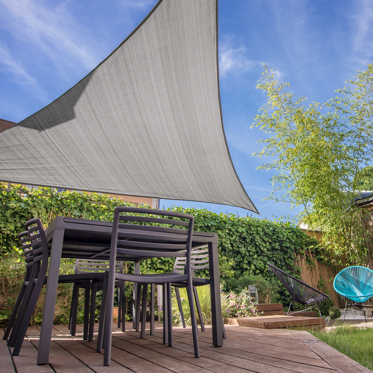 Garden with a gray triangular sunshade over a table and chairs.