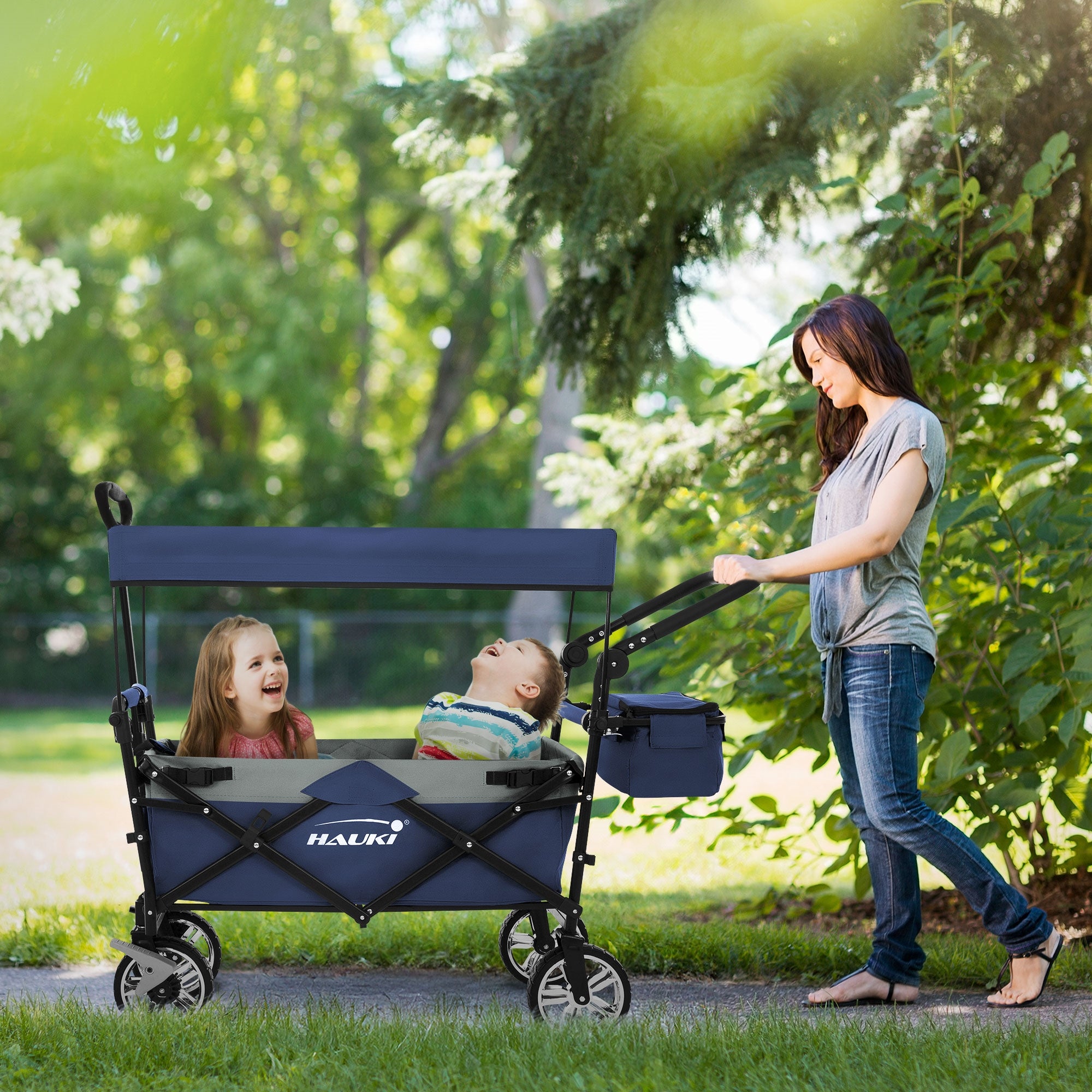 Eine Frau schiebt einen Kinderwagen mit zwei Kindern im Park.