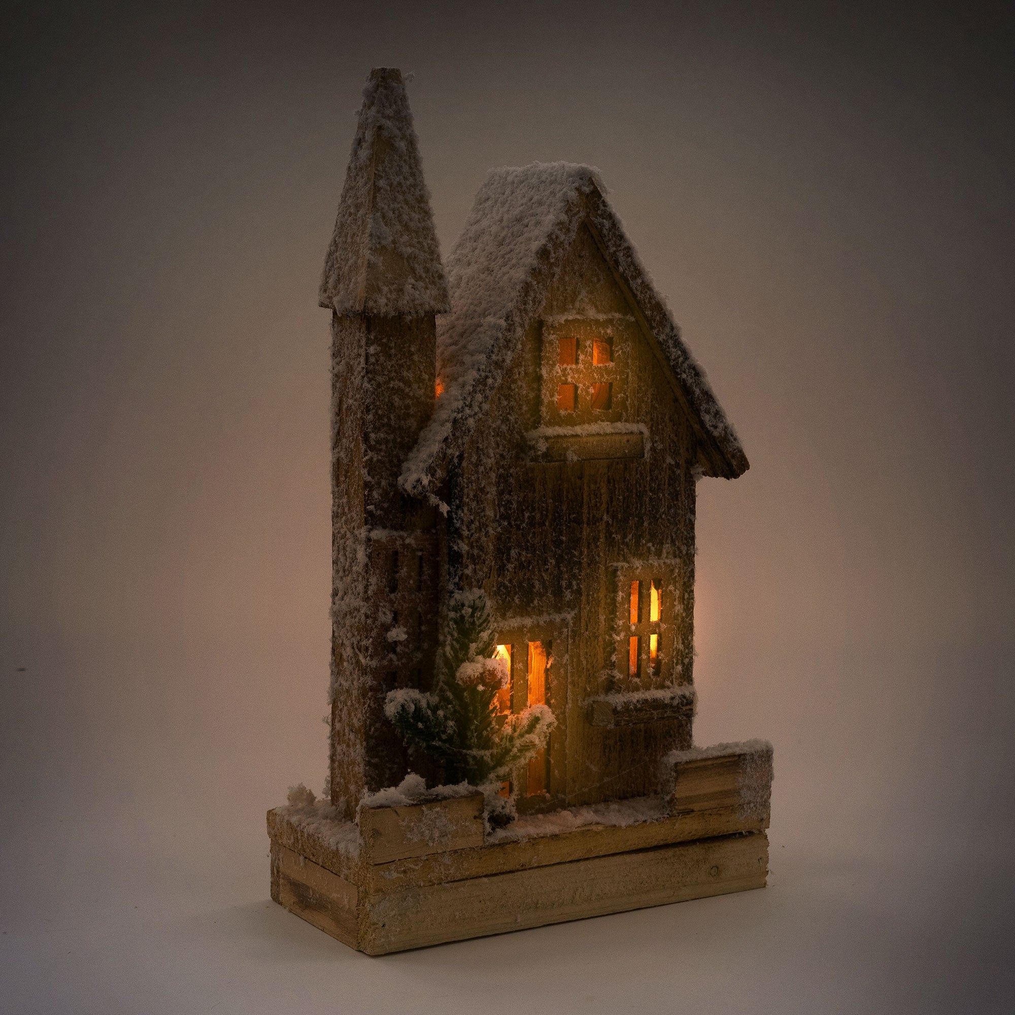 Beleuchtetes Holzhaus mit Schnee, warmem Licht und Tannenbaum.