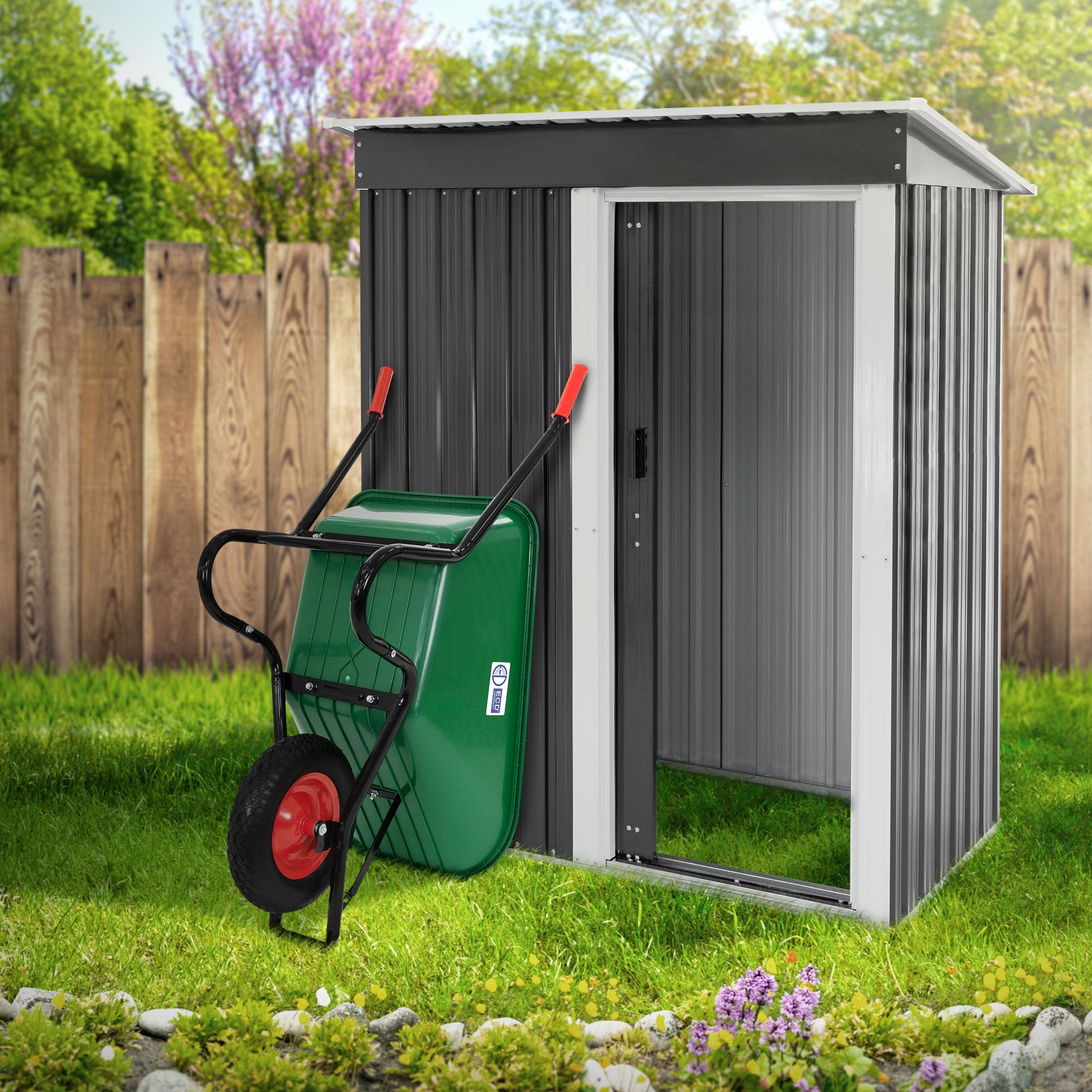 Groene tuinkar voor een tuinhuis met houten hek op de achtergrond.