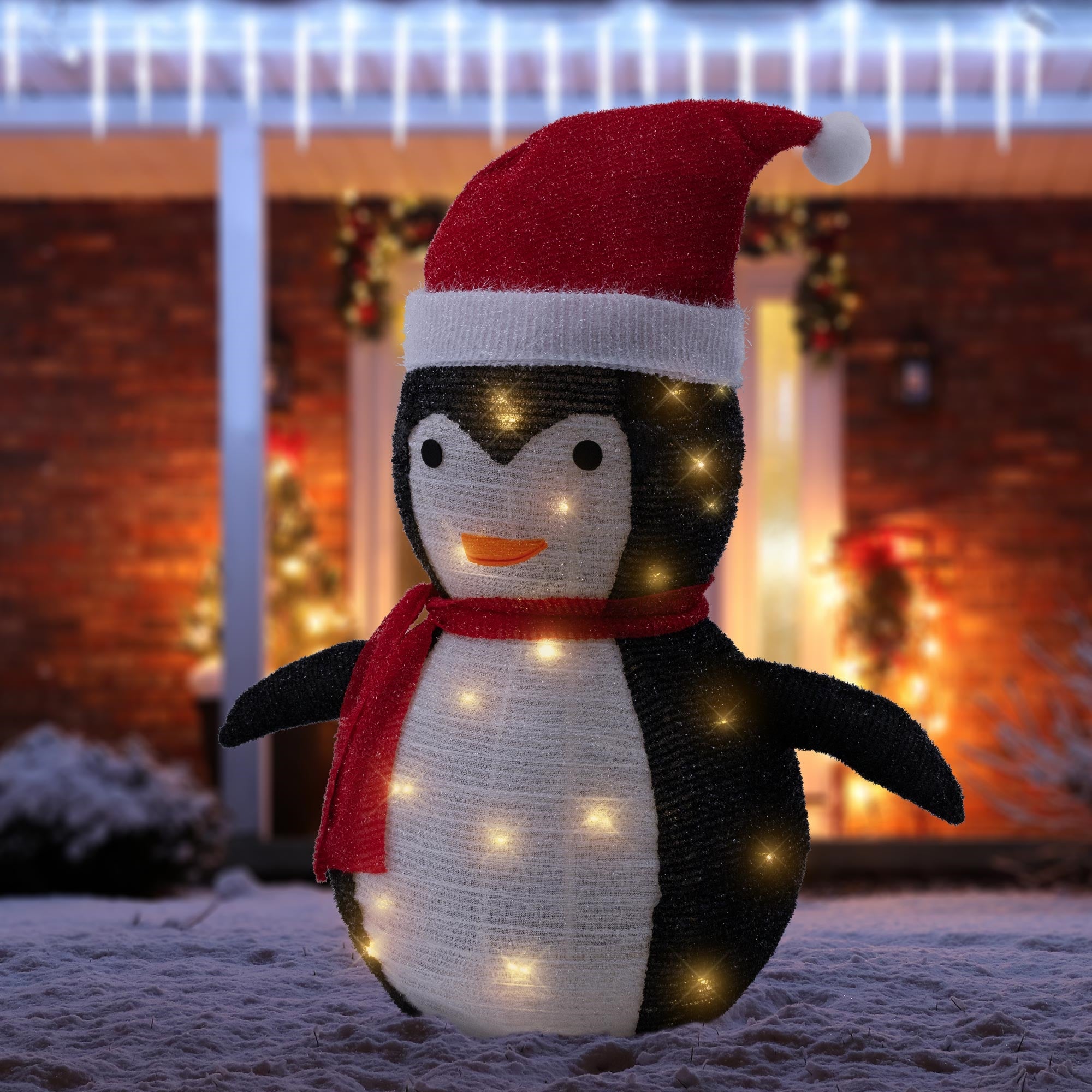 Loistava pingviini punaisella hatulla ja huivilla juhlallisesti koristellun talon edessä.