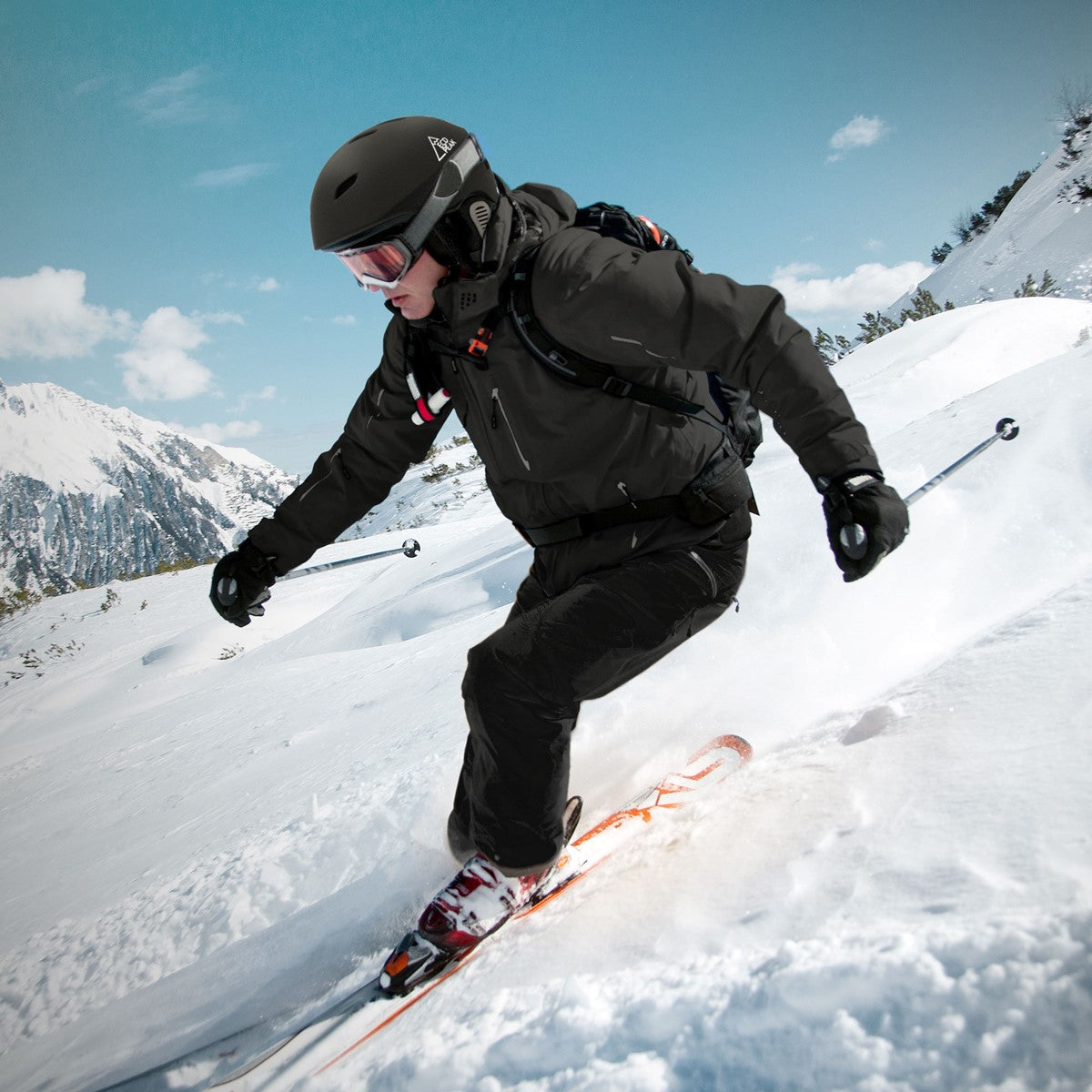 Skifahrer in schwarzer Ausrüstung fährt auf schneebedecktem Hang mit Bergen im Hintergrund.