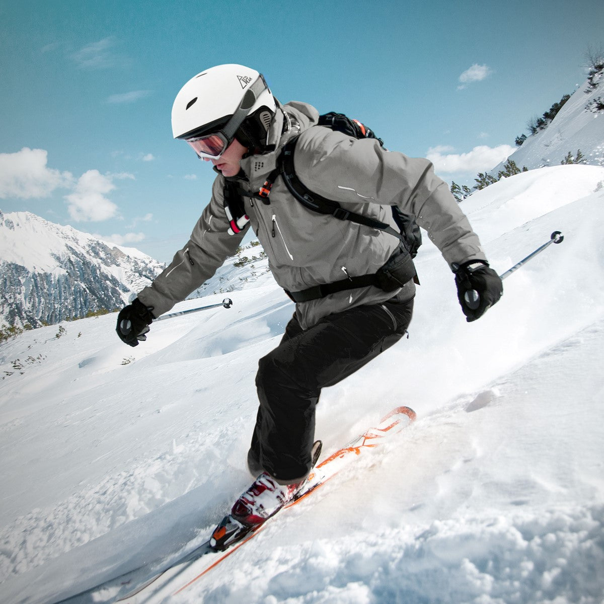 Skifahrer in grauer Jacke fährt durch verschneite Landschaft.