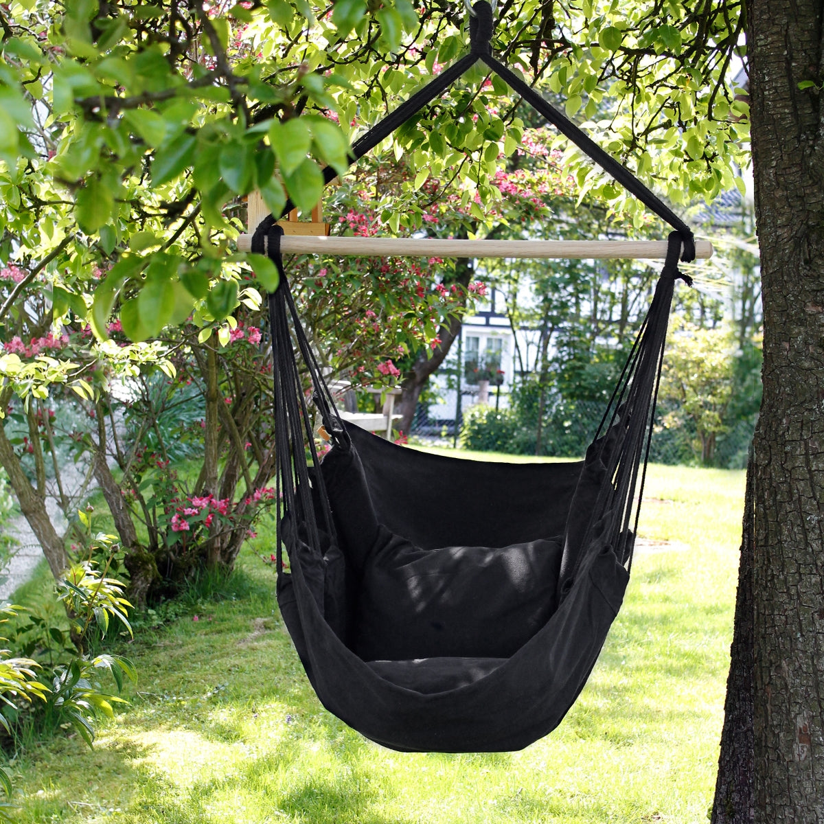 Poltrona a dondolo nera, appesa sotto un albero in un giardino.