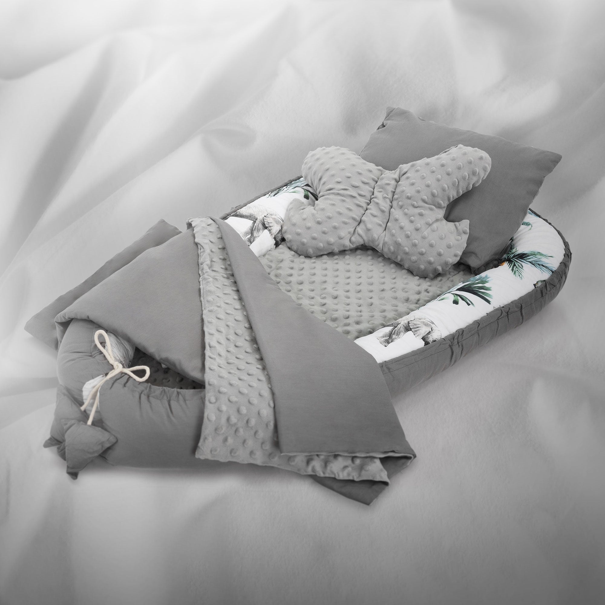 Un lit pour bébé gris avec un coussin en forme de papillon et une couverture avec motif de palmiers.