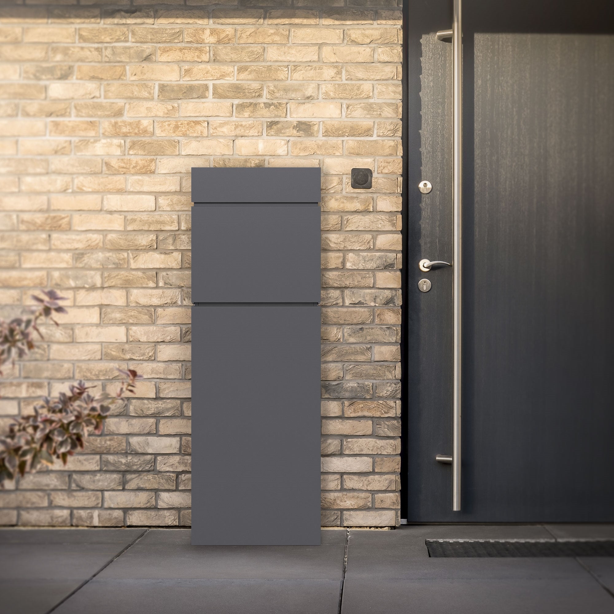 A gray mailbox in front of a brick wall and a door.