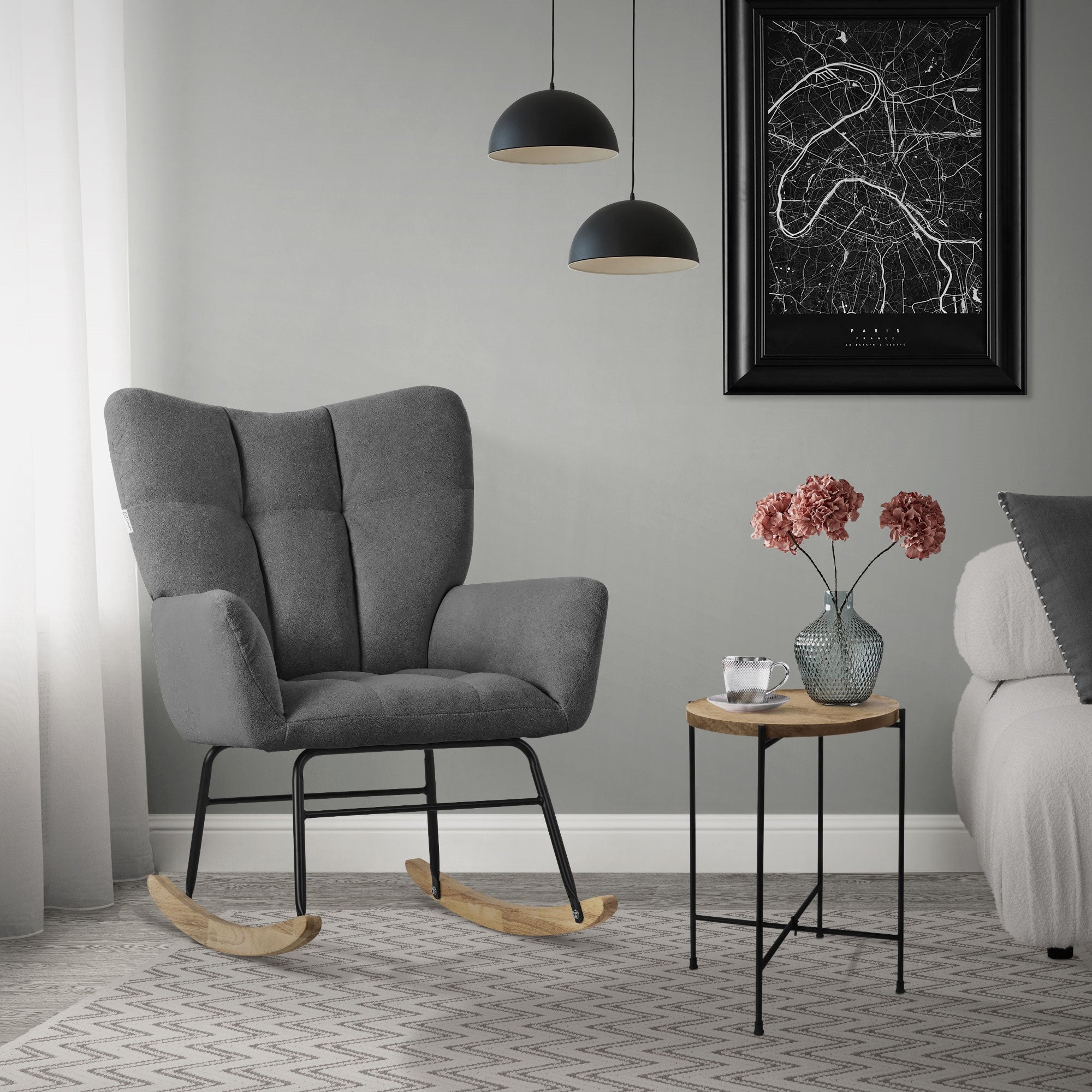 Un fauteuil à bascule gris se tient à côté d'une petite table avec des fleurs et une lampe.