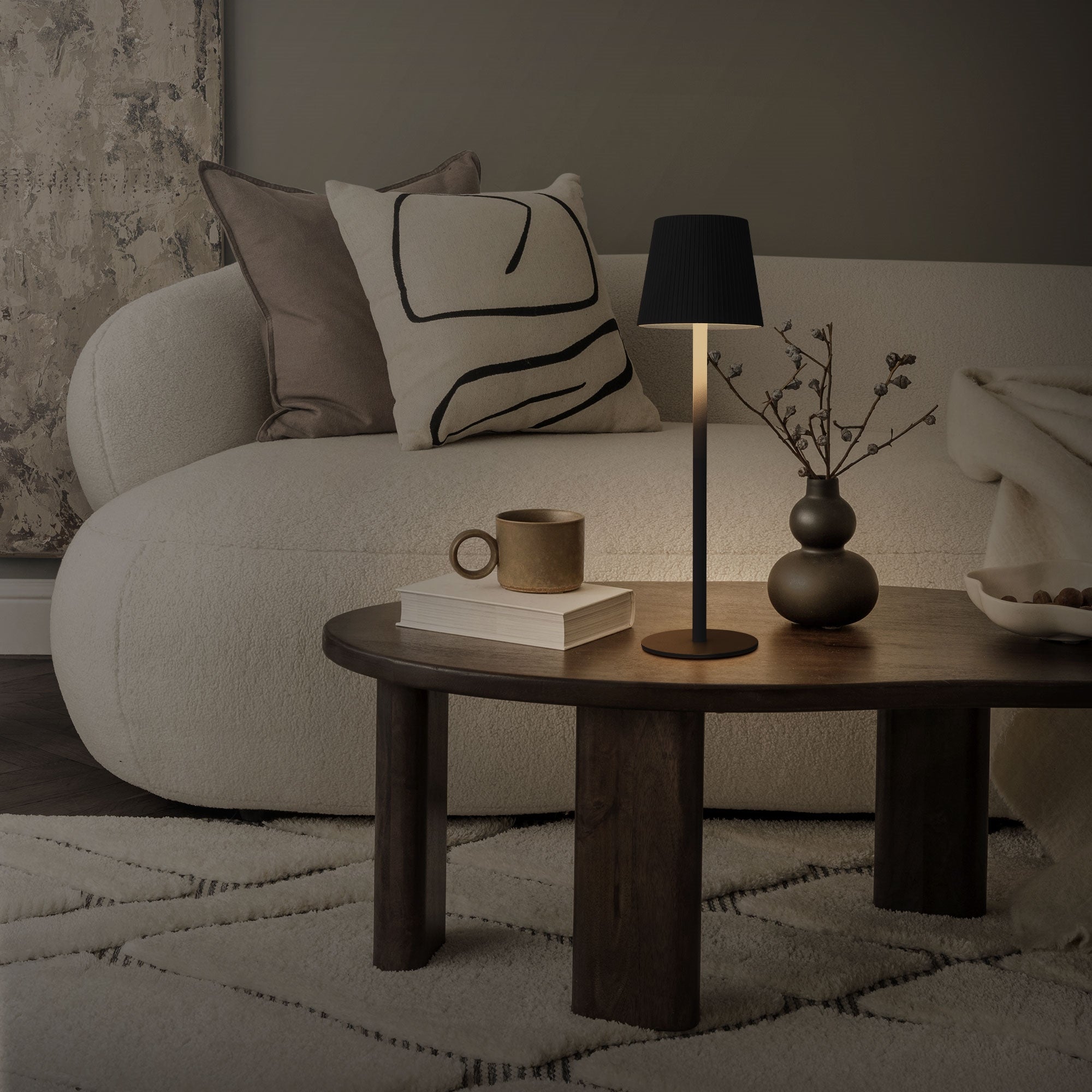 Ein Wohnzimmer mit einem Sofa, einem Tisch, einer Lampe und einer Vase auf dem Tisch.