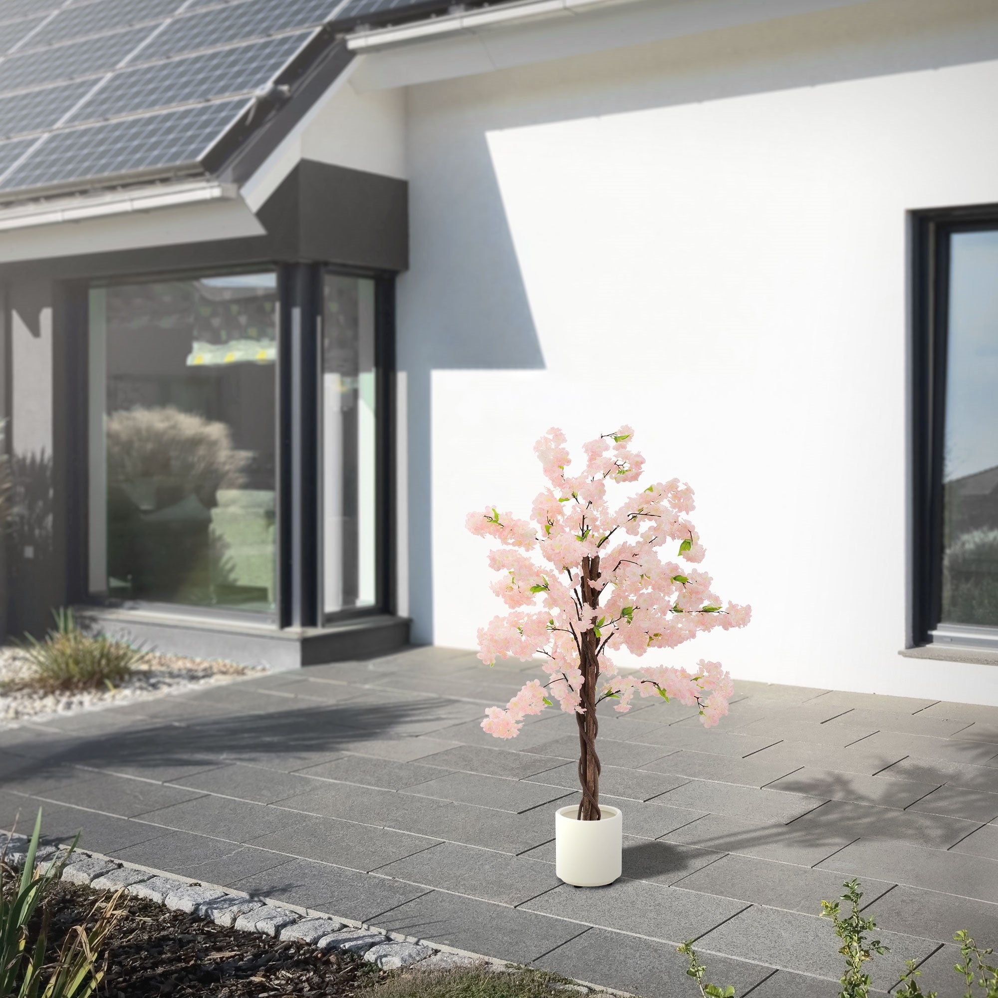 Kunstbaum mit rosa Blüten vor einem modernen Haus mit Solarpanelen.