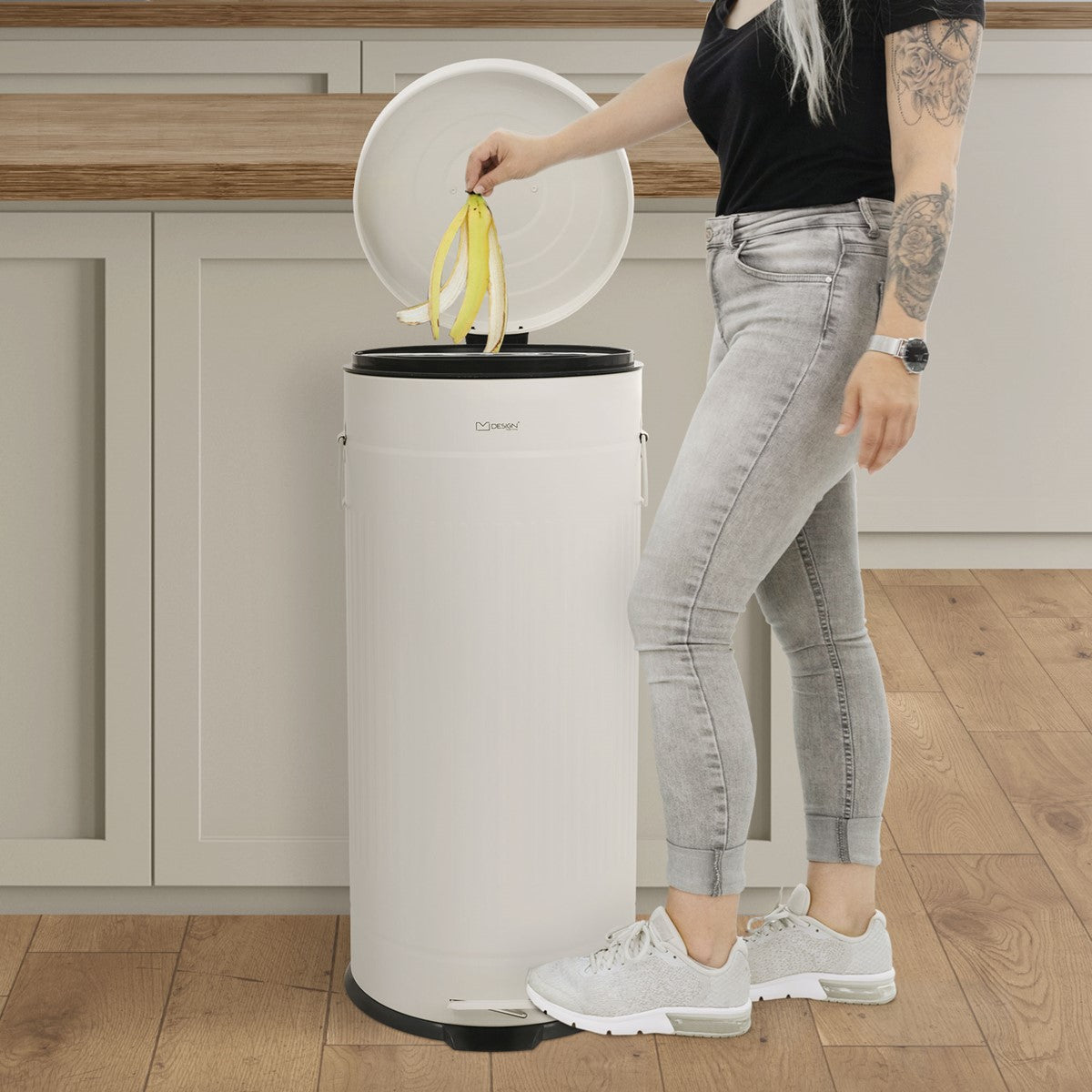 Person mit langen Haaren wirft Bananenschalen in eine weiße Mülltonne.