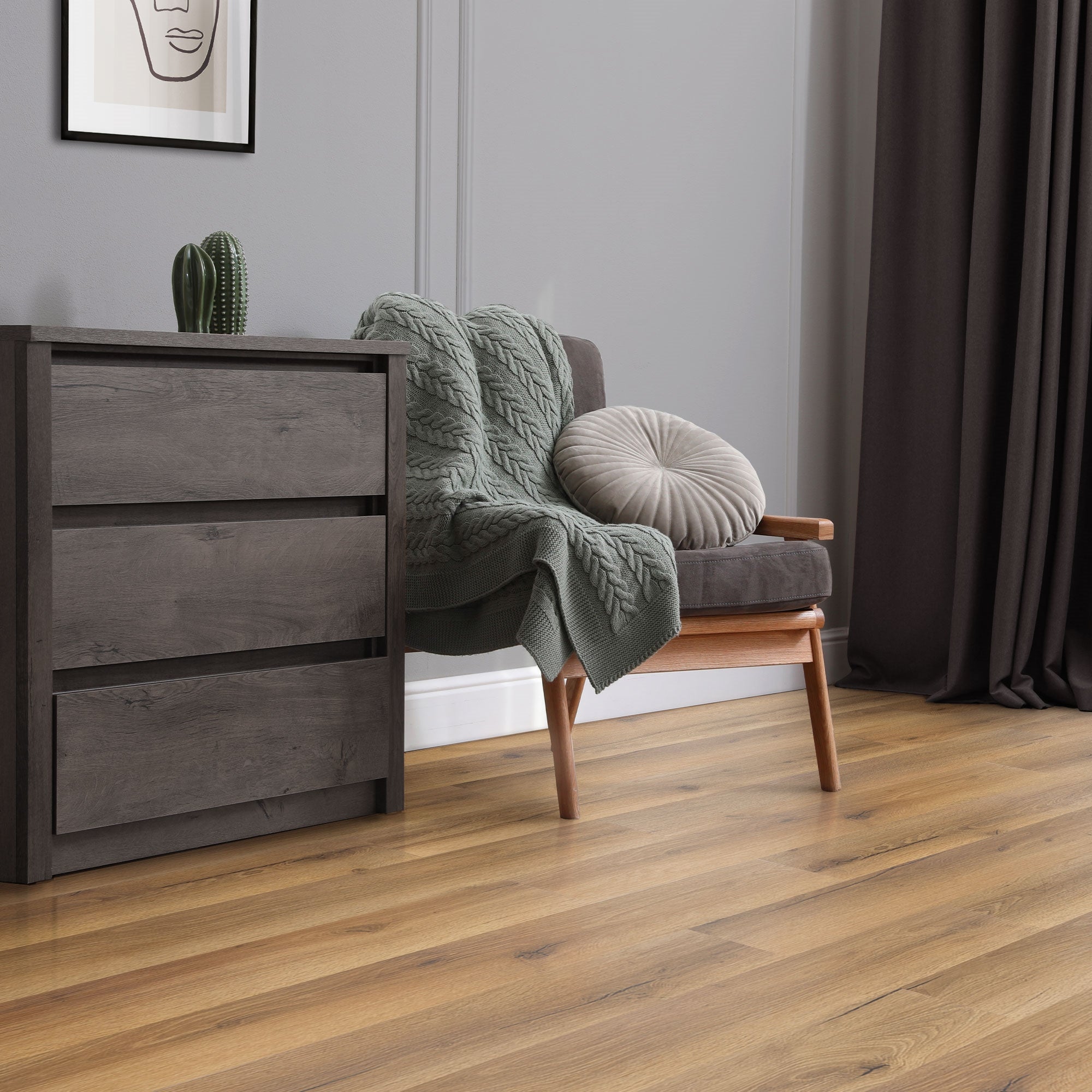 Een grijze bank met een deken en een kussen, houten kast en plant op de achtergrond.
