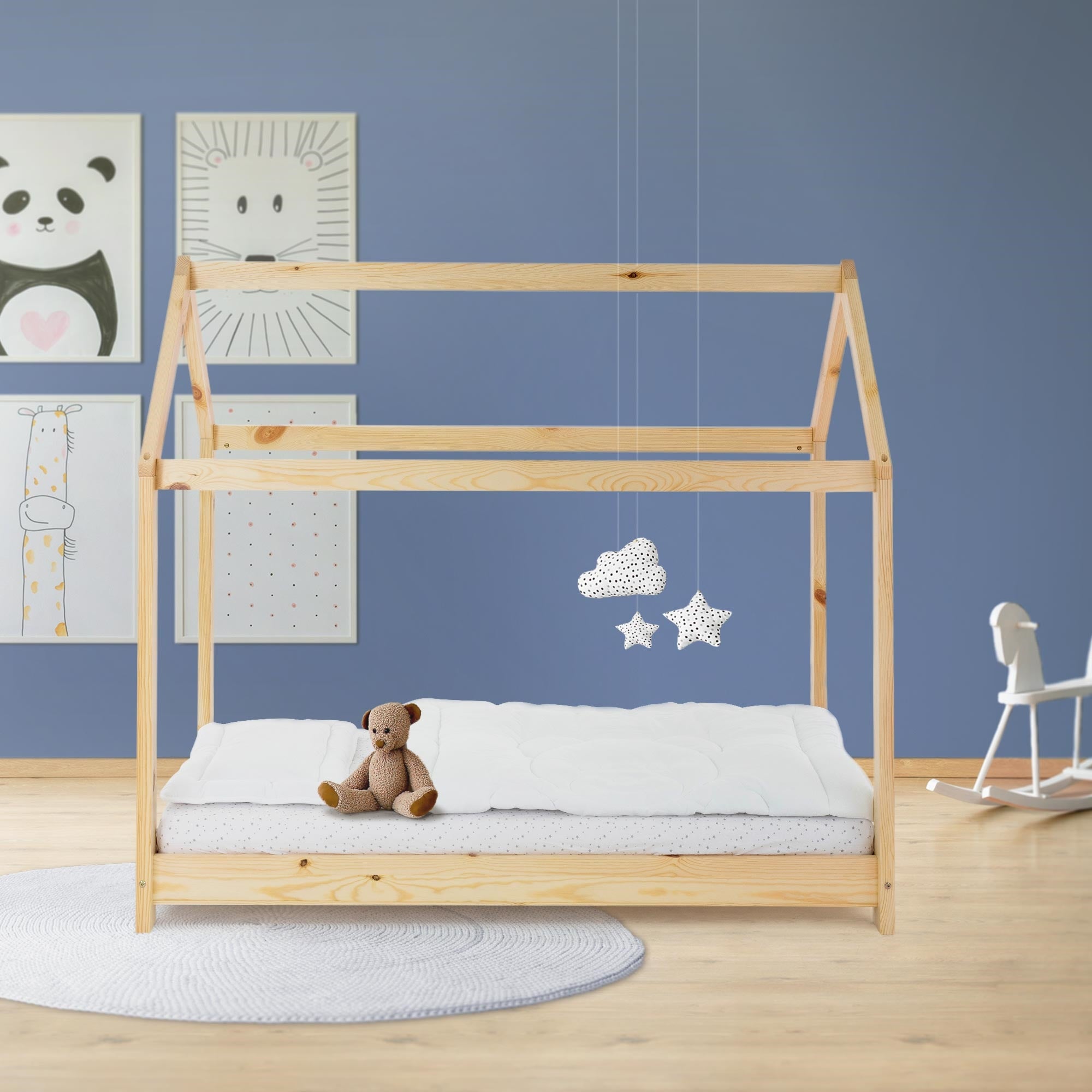 Wooden children's bed with teddy bear and clouds, against a blue wall with pictures.