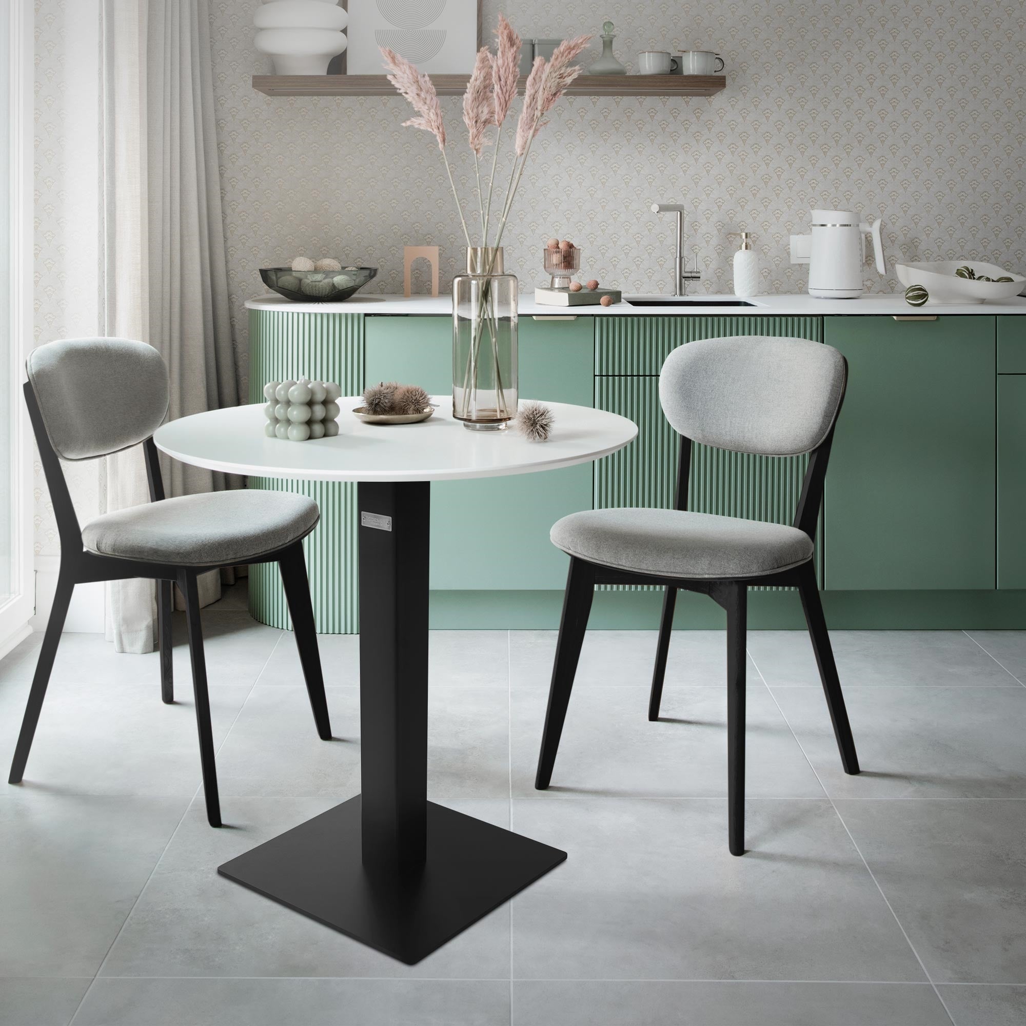 Un tavolo rotondo con due sedie in una cucina luminosa, decorato con piante.