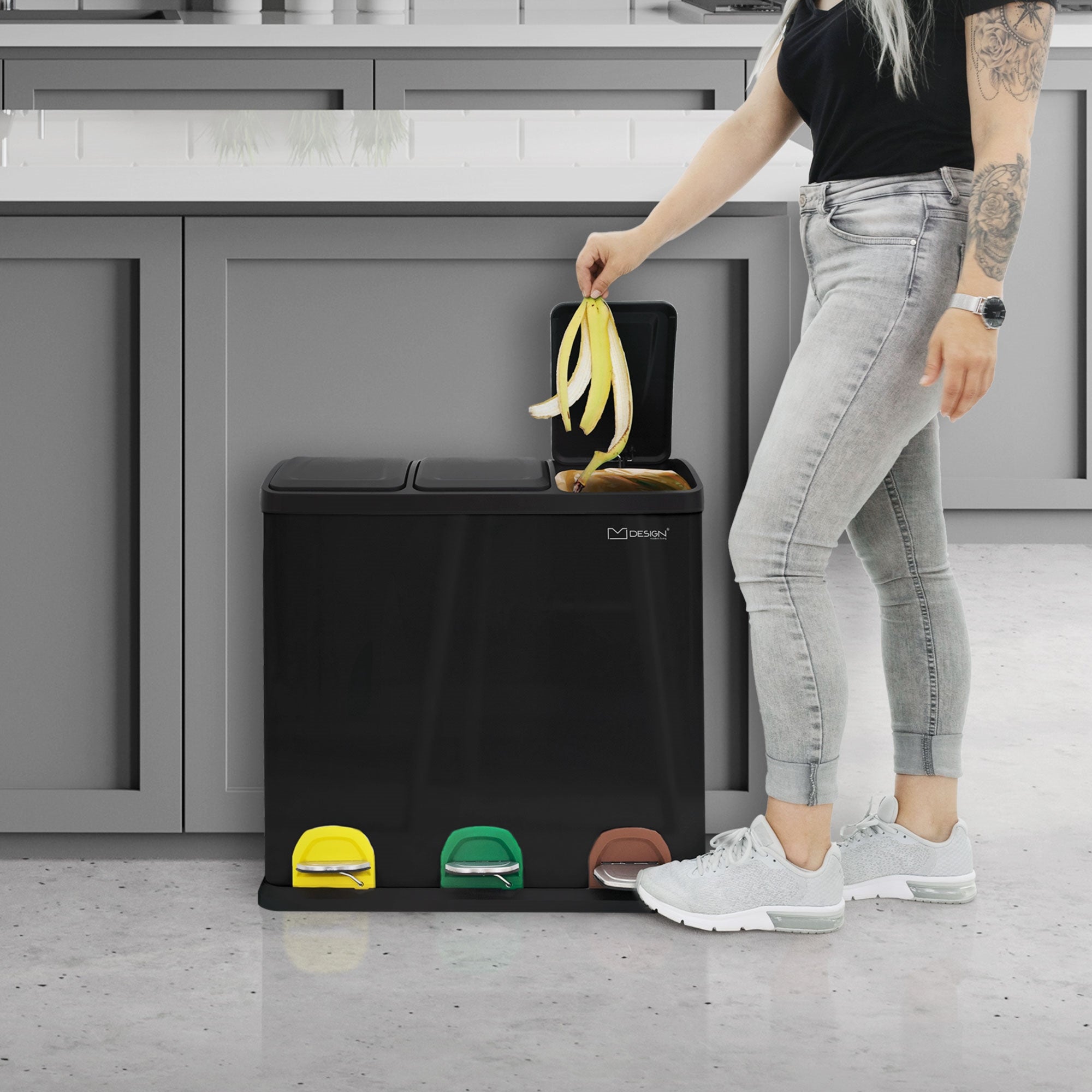 Person mit langen Haaren, die eine Banane in einen Mülleimer mit drei Fächern wirft.