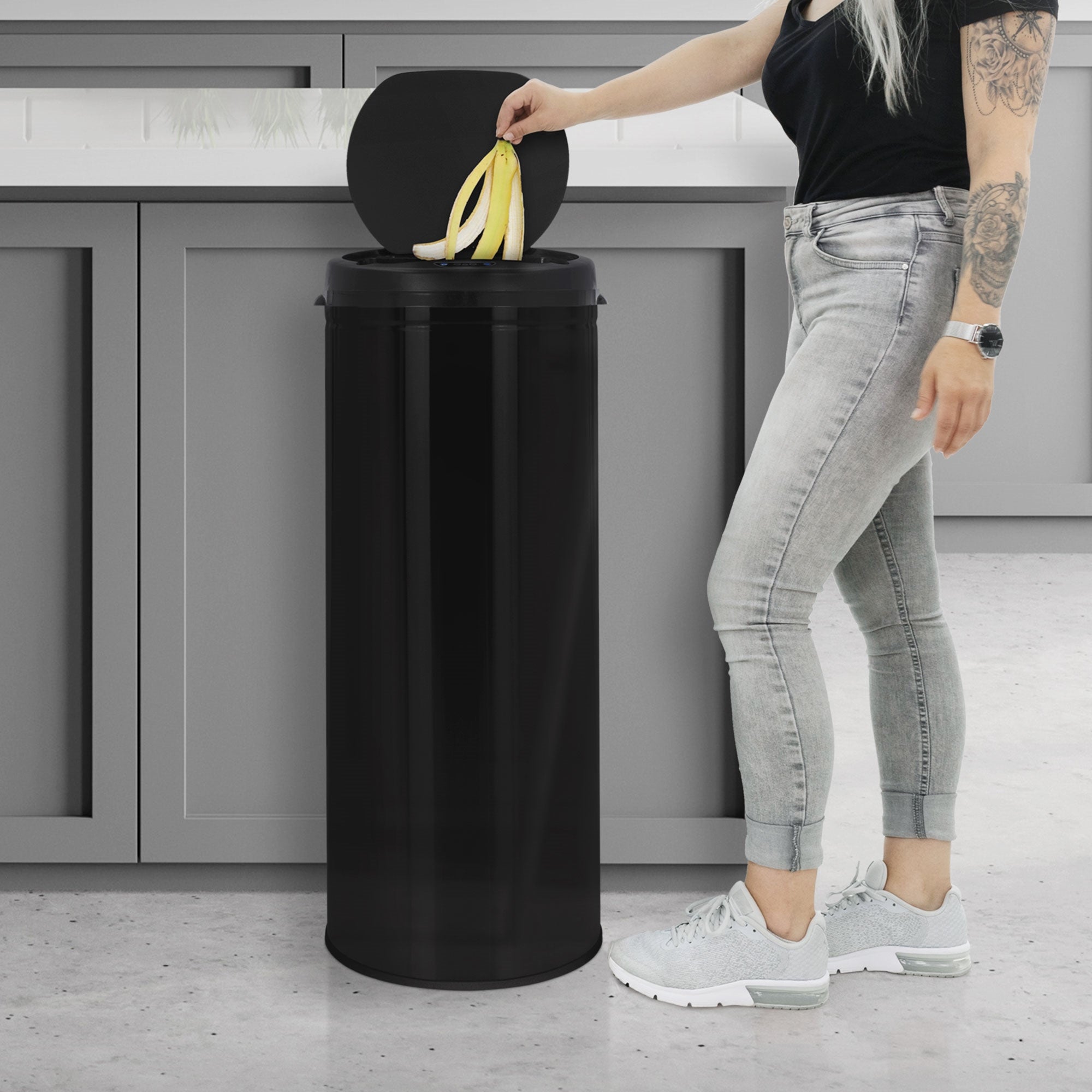 Une personne jette des bananes dans une poubelle noire dans une cuisine moderne.