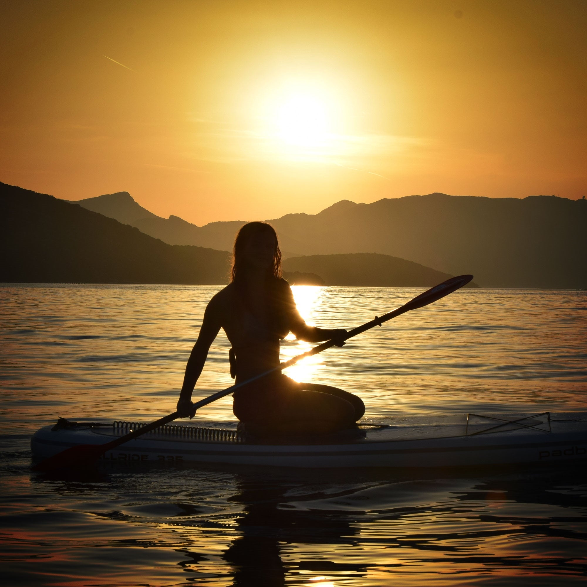 Silhouette d'une personne sur un kayak au coucher du soleil, avec de l'eau au premier plan.