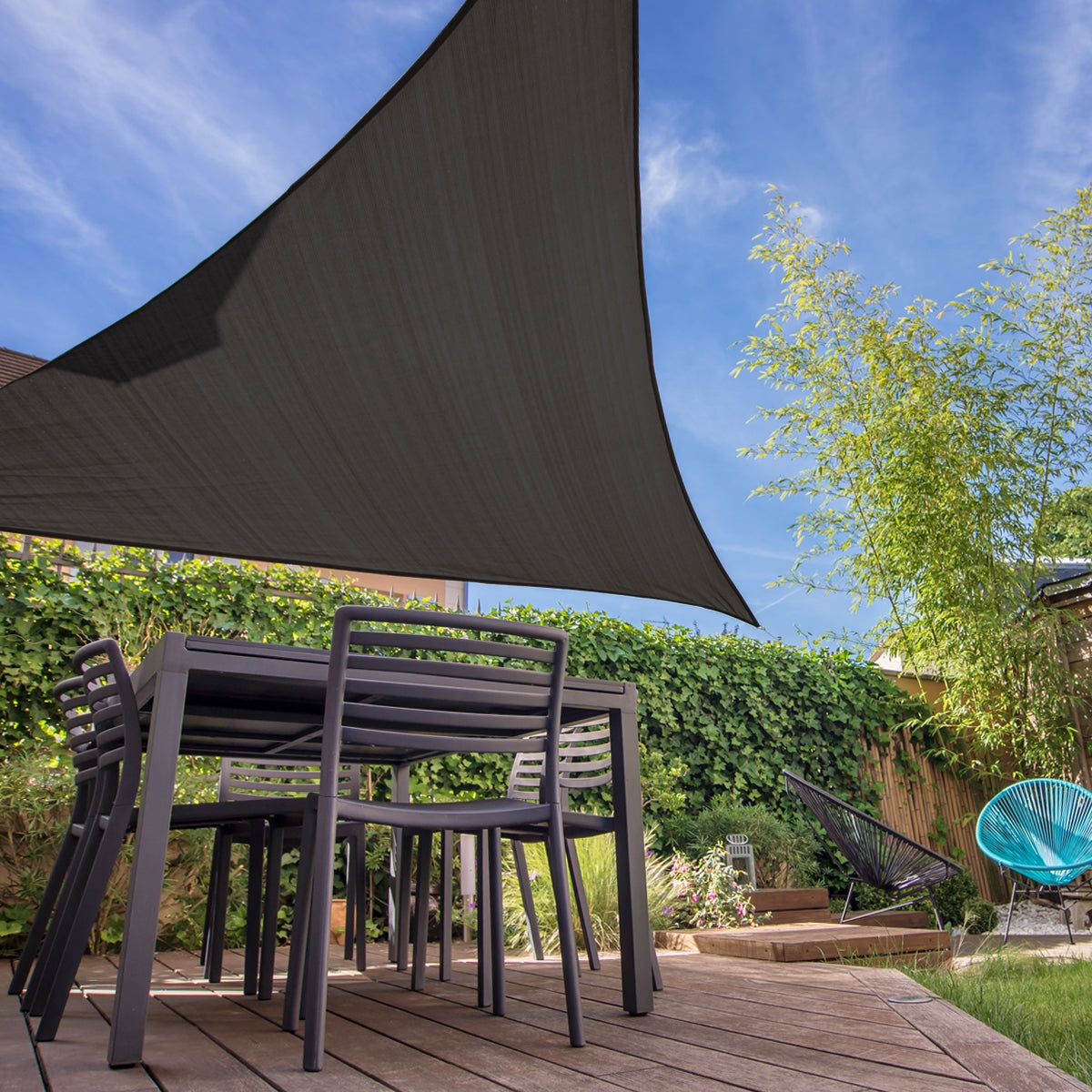 Jardin avec un voile d'ombrage triangulaire anthracite au-dessus d'une table et de chaises.