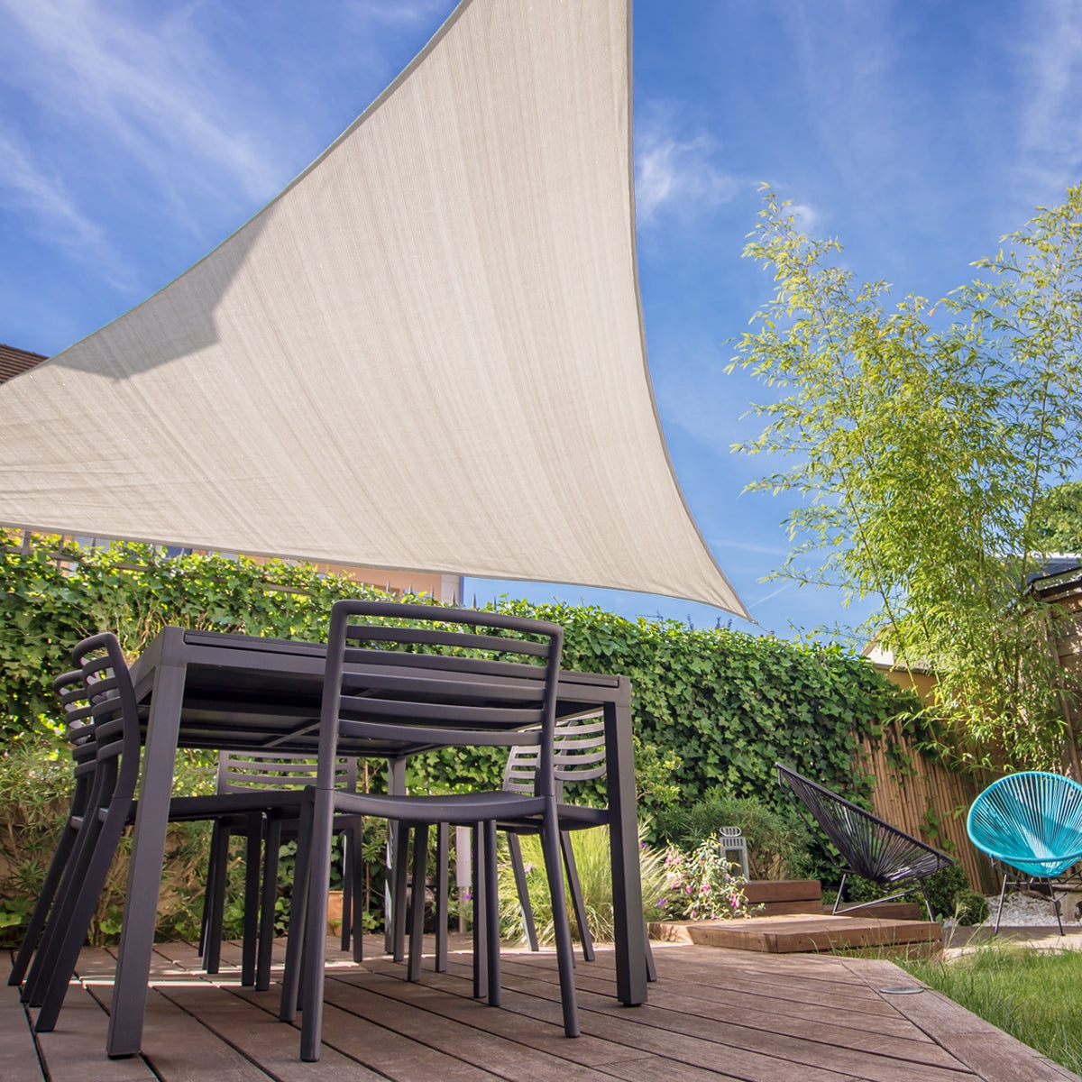 Garden with a cream-colored triangular sun sail over a table and chairs.