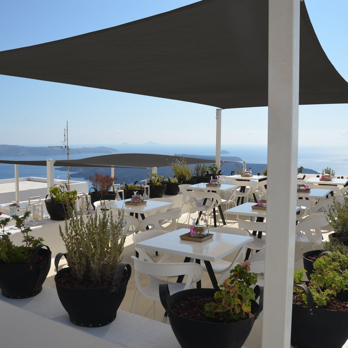 Terrazza con tavoli, piante e un grande telo da sole antracite.