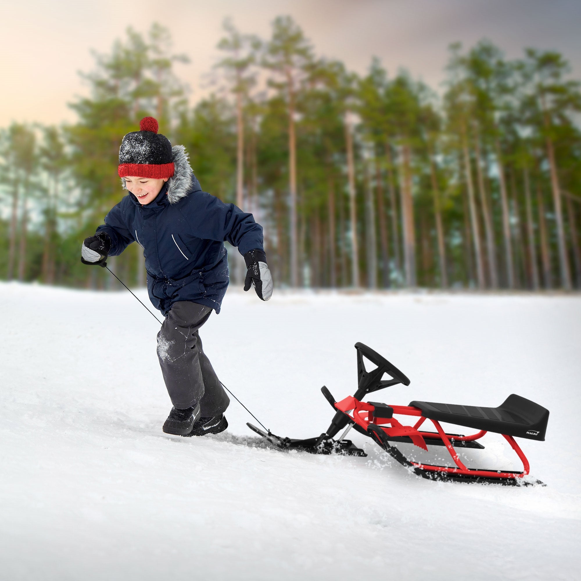 Enfant tirant une luge rouge dans la neige, entouré d'arbres.