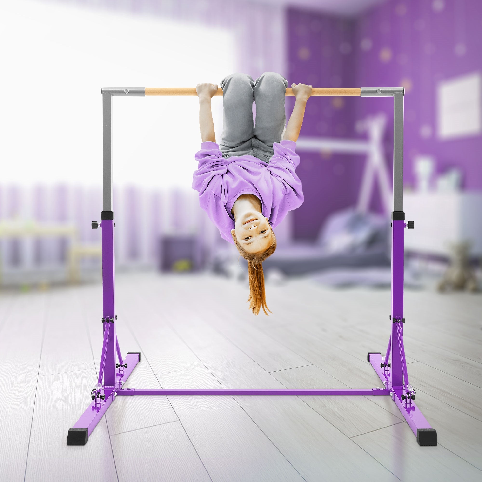 Child hanging on a purple gym apparatus, smiling and looking at the camera.