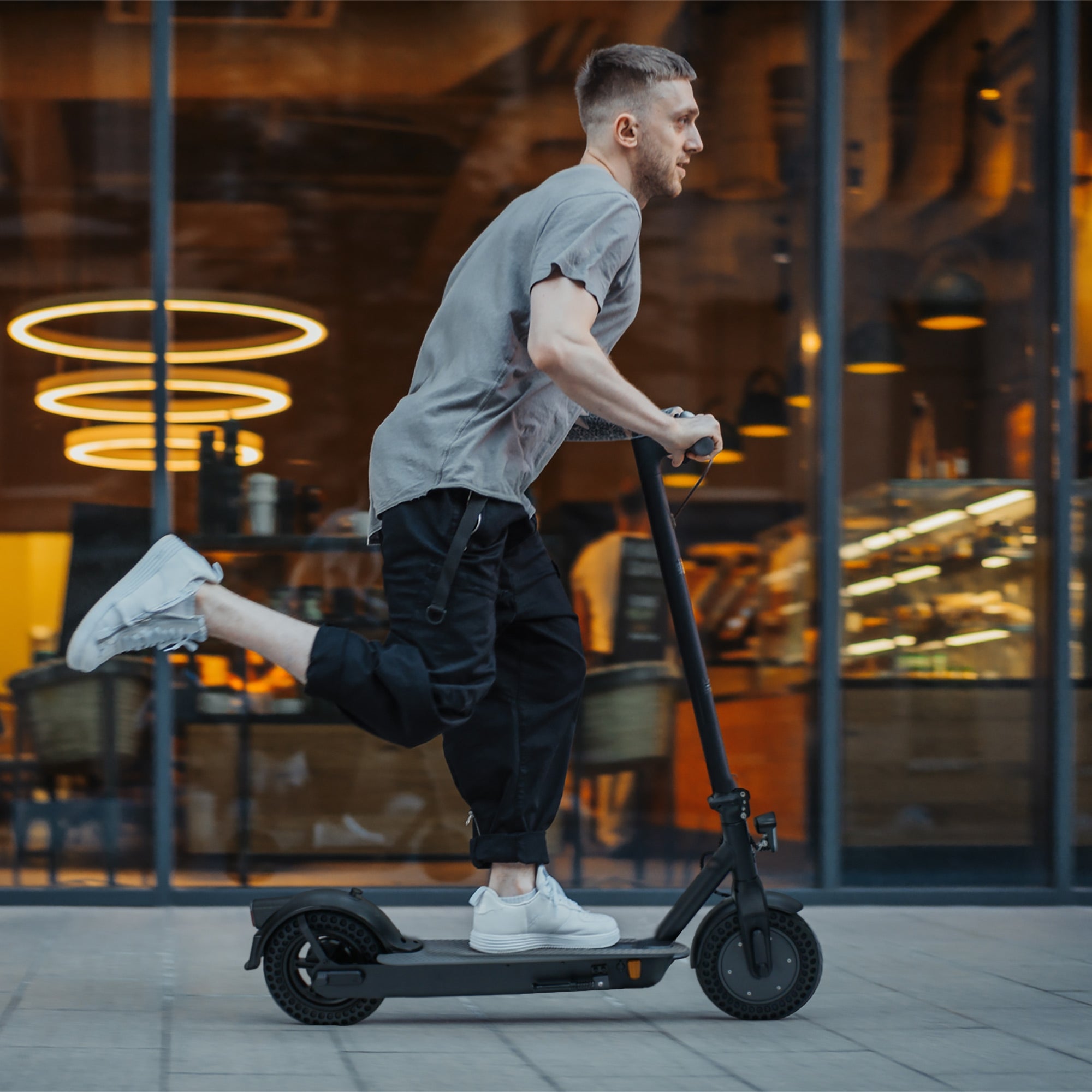 Mann fährt auf E-Scooter in urbaner Umgebung, Café im Hintergrund.