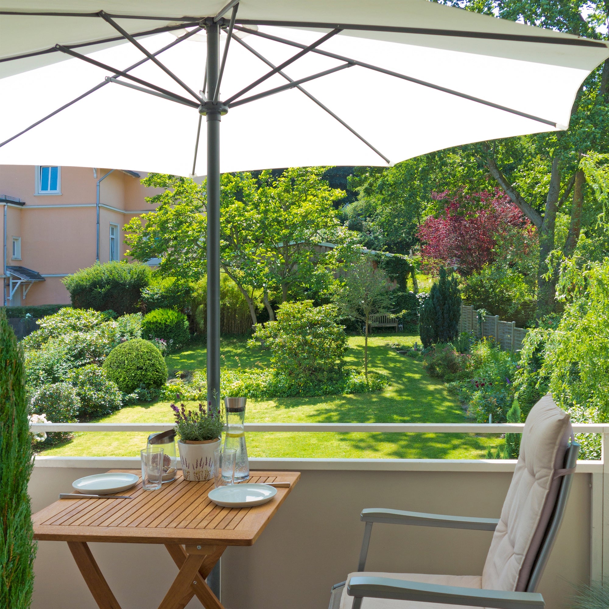 Terraza con una sombrilla, mesa y sillas, rodeada de un jardín.