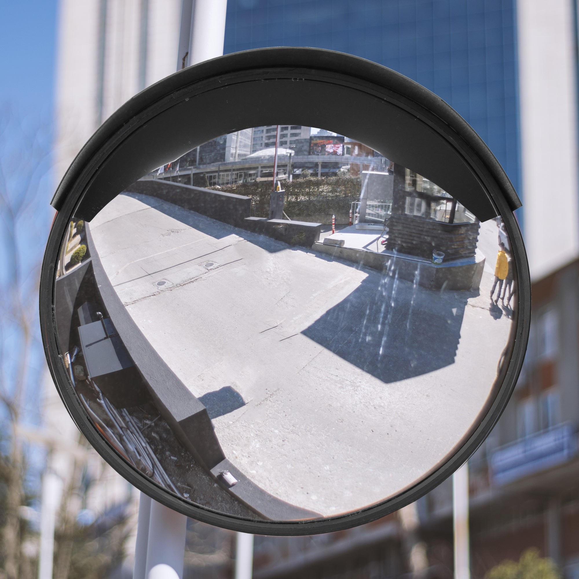 Runder Verkehrsspiegel mit Reflexion einer Straße und Gebäuden im Hintergrund.