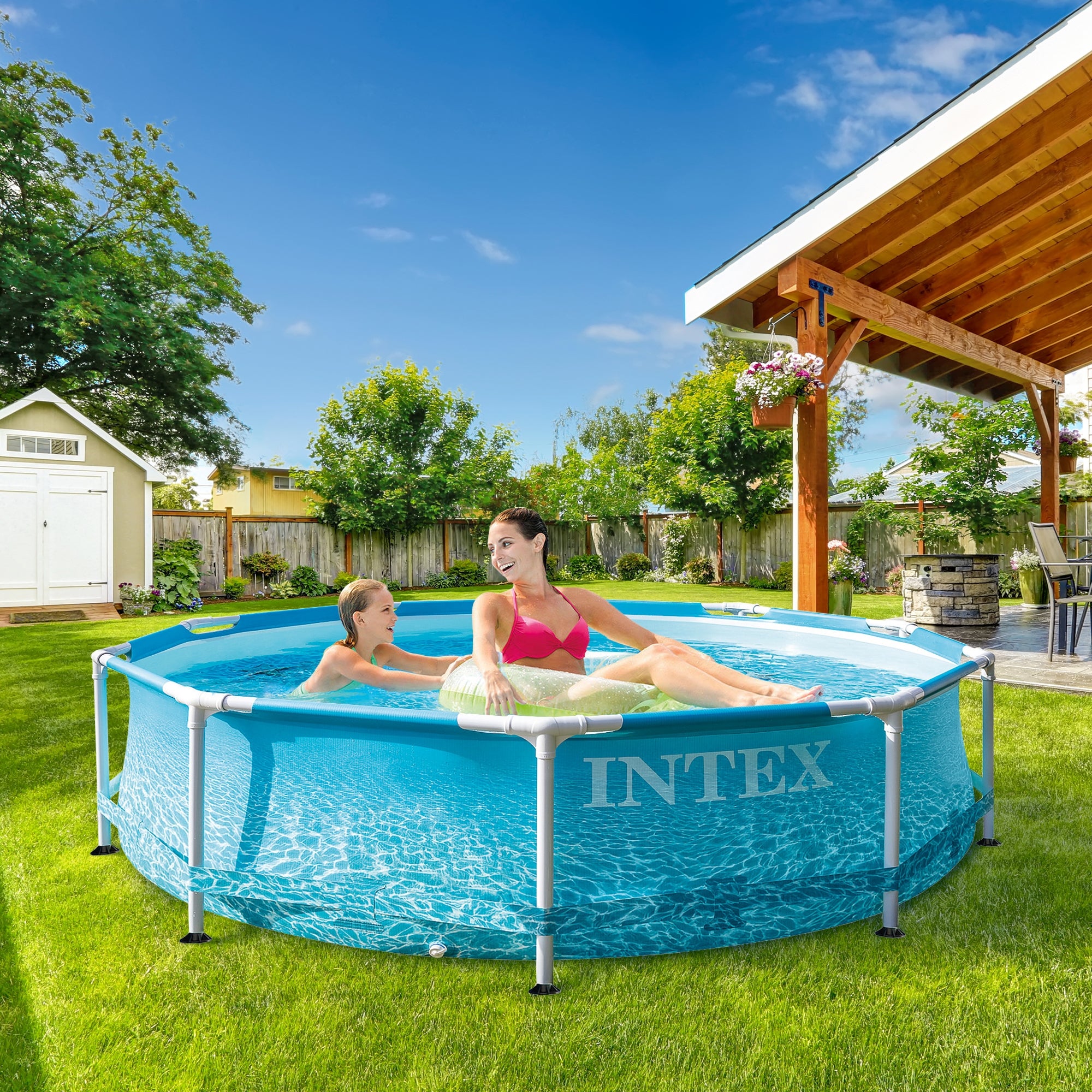 Two people in the pool on a lawn, surrounded by trees and a wooden overhang.