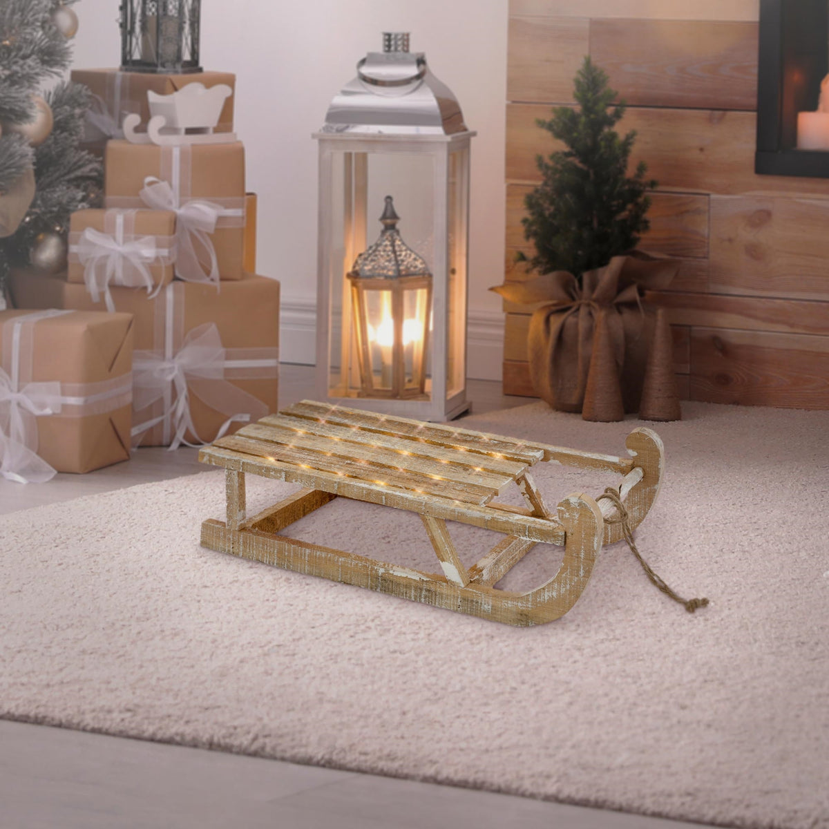Une luge en bois est posée sur un tapis devant une lanterne et un sapin de Noël.