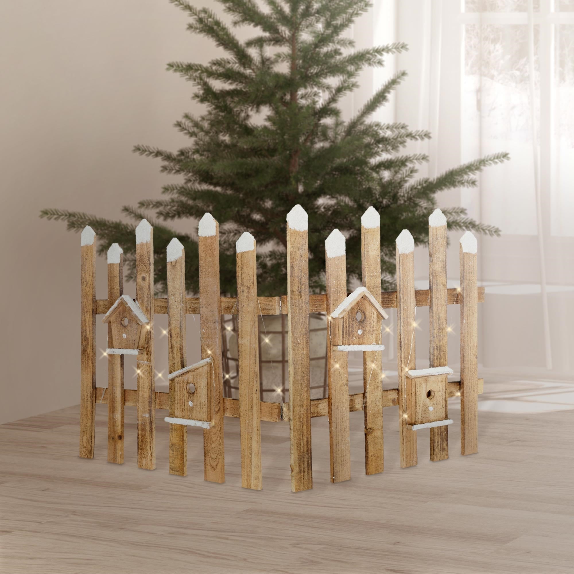 Holzfarbener Zaun mit weißen Spitzen, um einen Weihnachtsbaum.