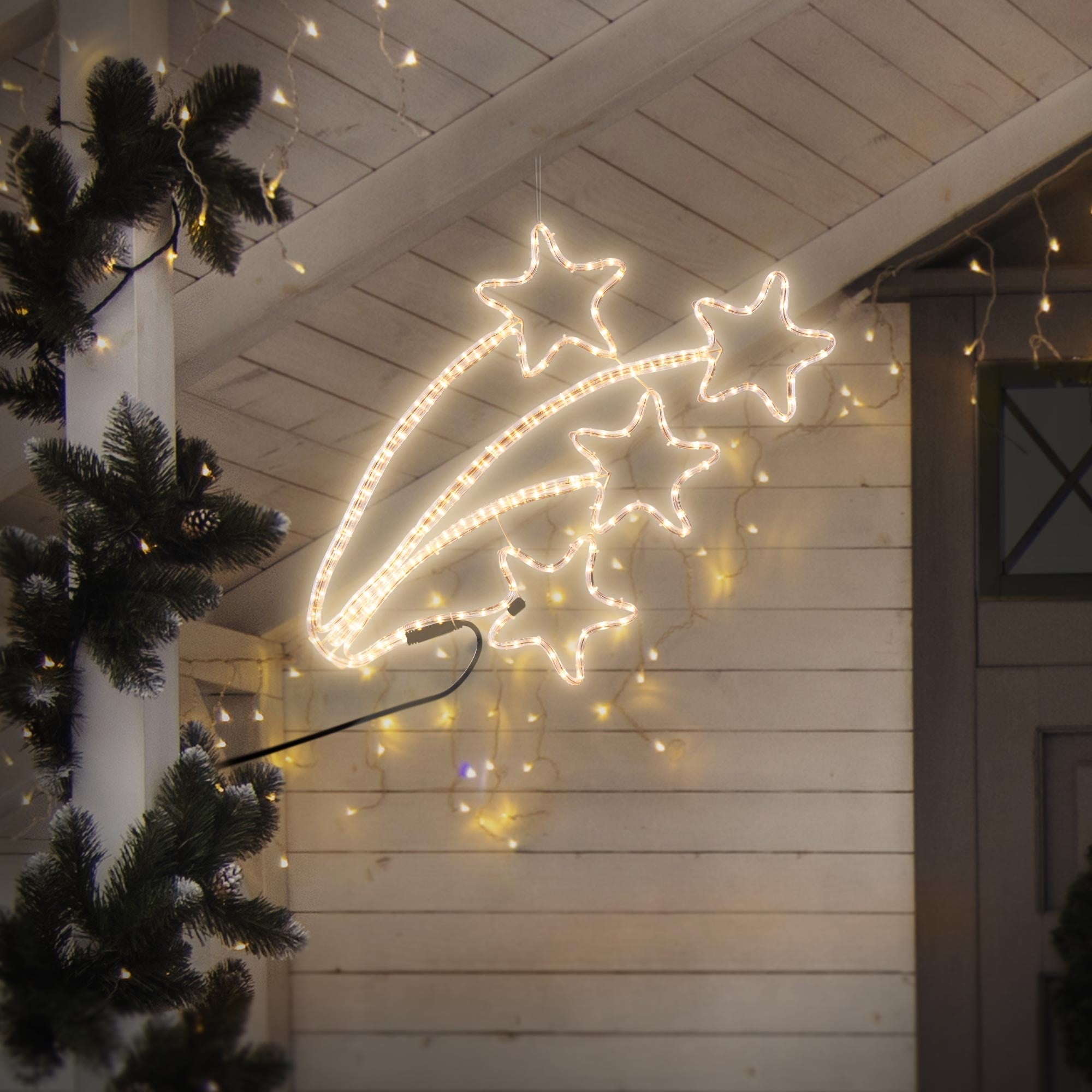 Stelle luminose di luci appese a un tetto, circondate da rami di abete.