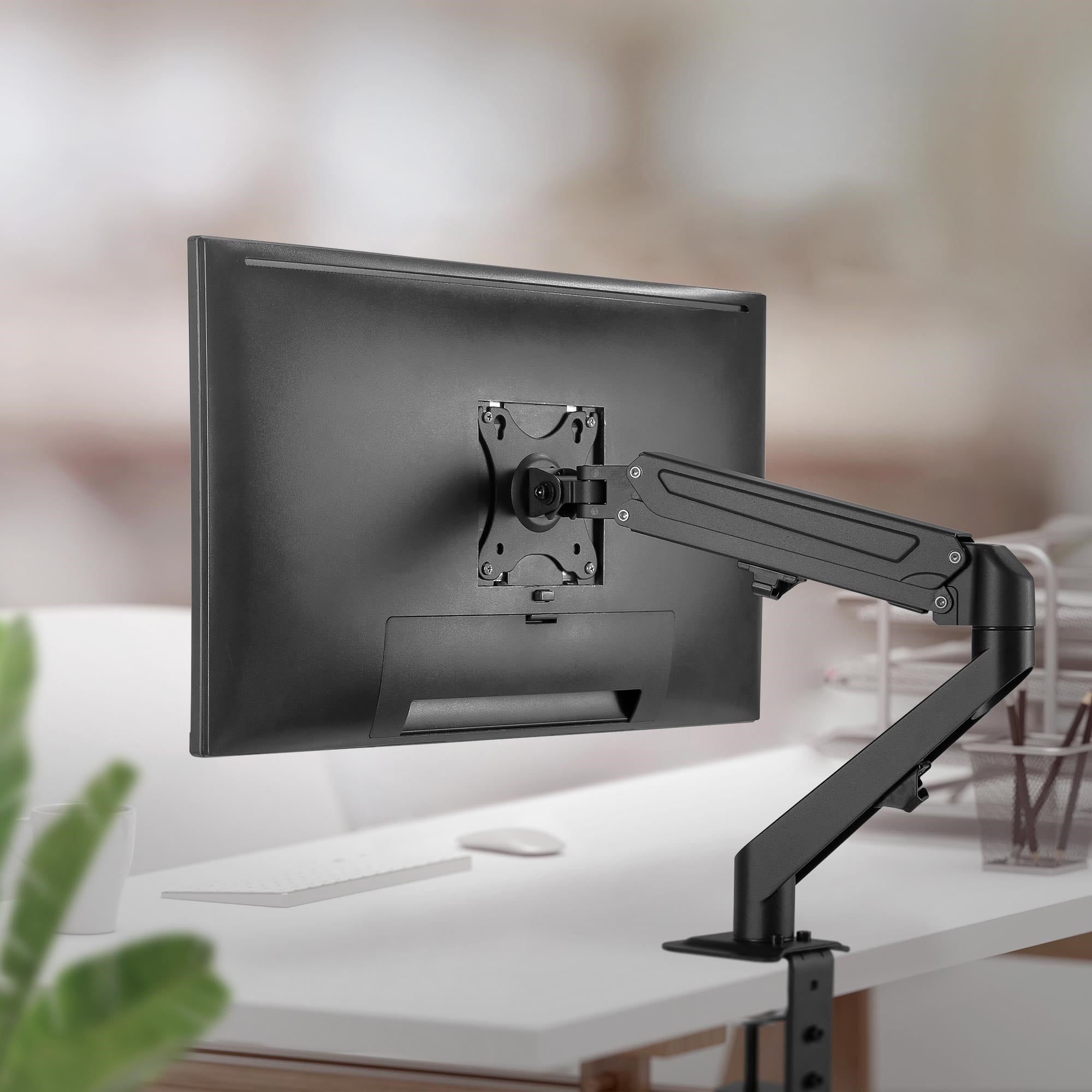 Monitor na uchwycie, na biurku z klawiaturą.