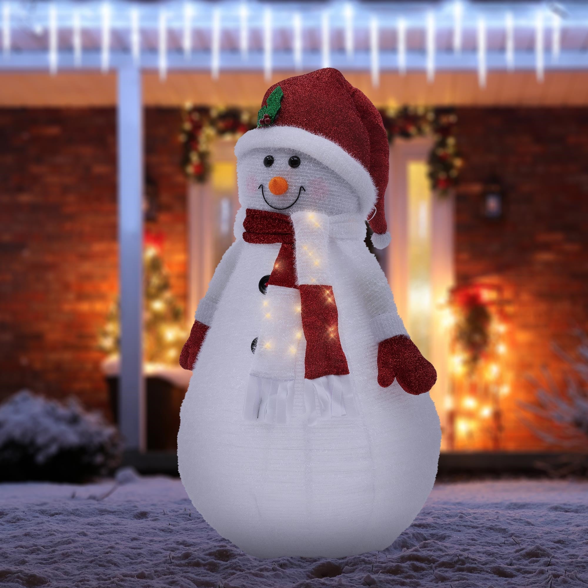 Bonhomme de neige éclairé avec un chapeau rouge et une écharpe dans la neige.