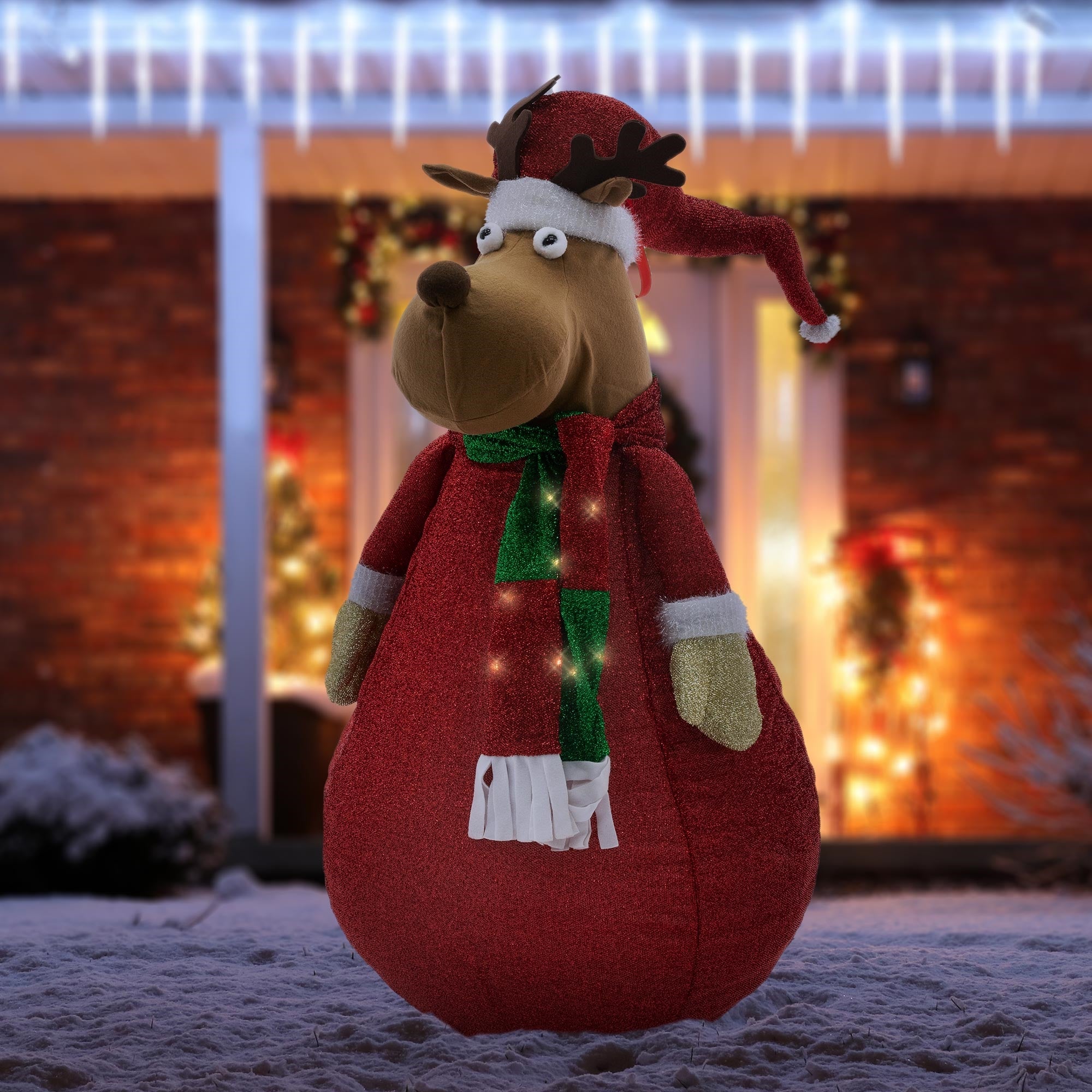 Renne en peluche dans une décoration de Noël dans la neige, avec des lumières en arrière-plan.