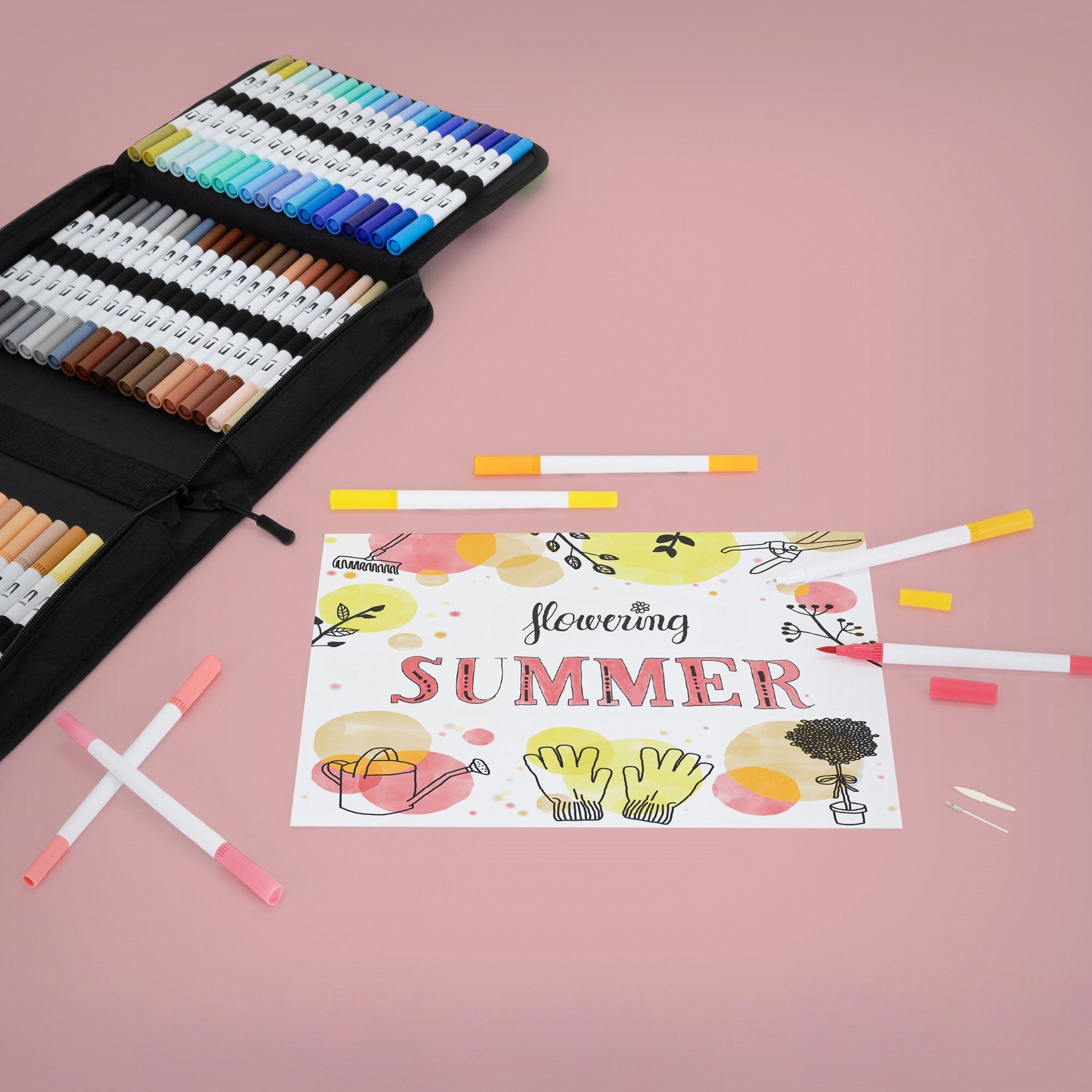 Farbenfrohe Marker und ein Blatt mit dem Text 'Flowering SUMMER' auf rosa Hintergrund.