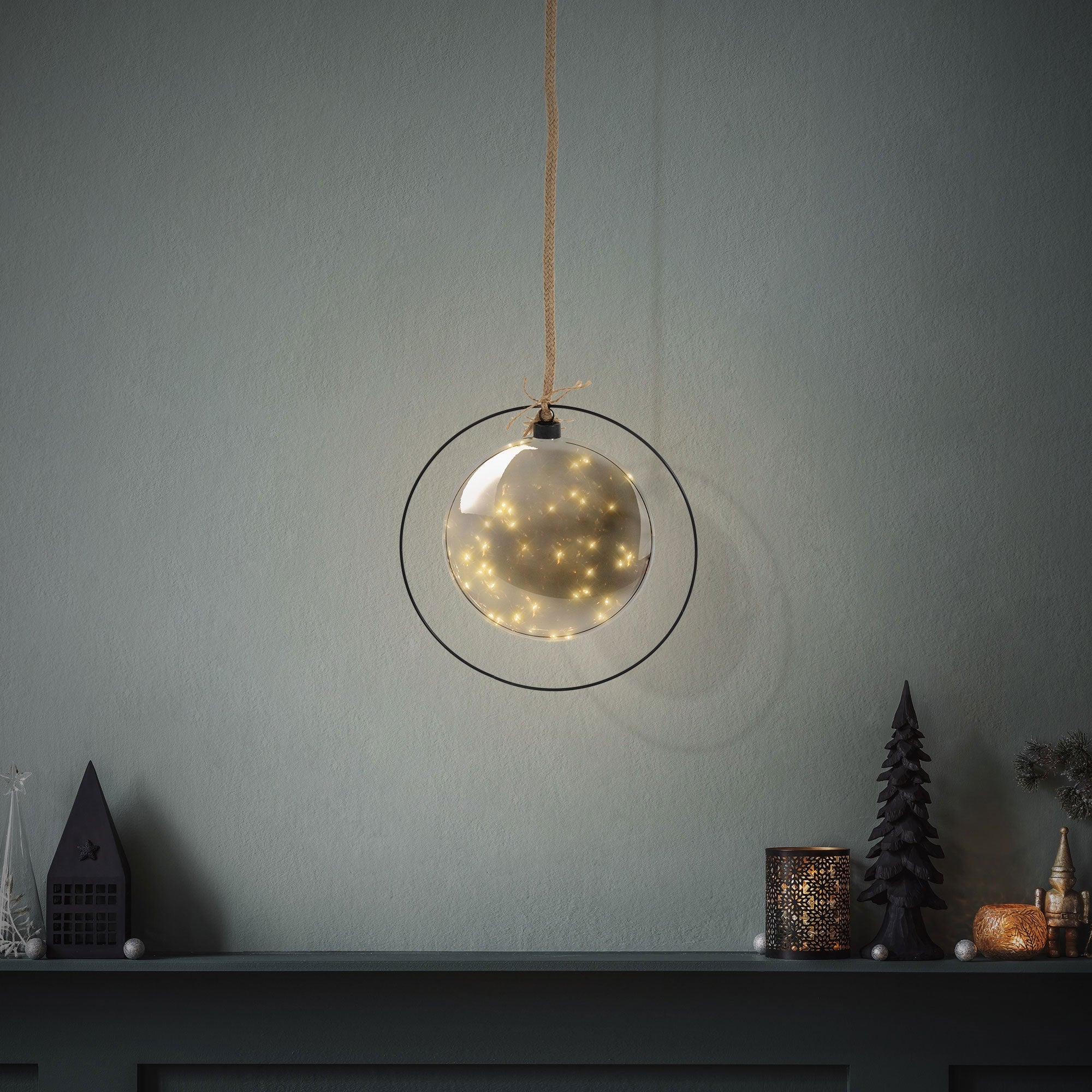 Hängende Glaskugel mit Lichtern vor einer grauen Wand.