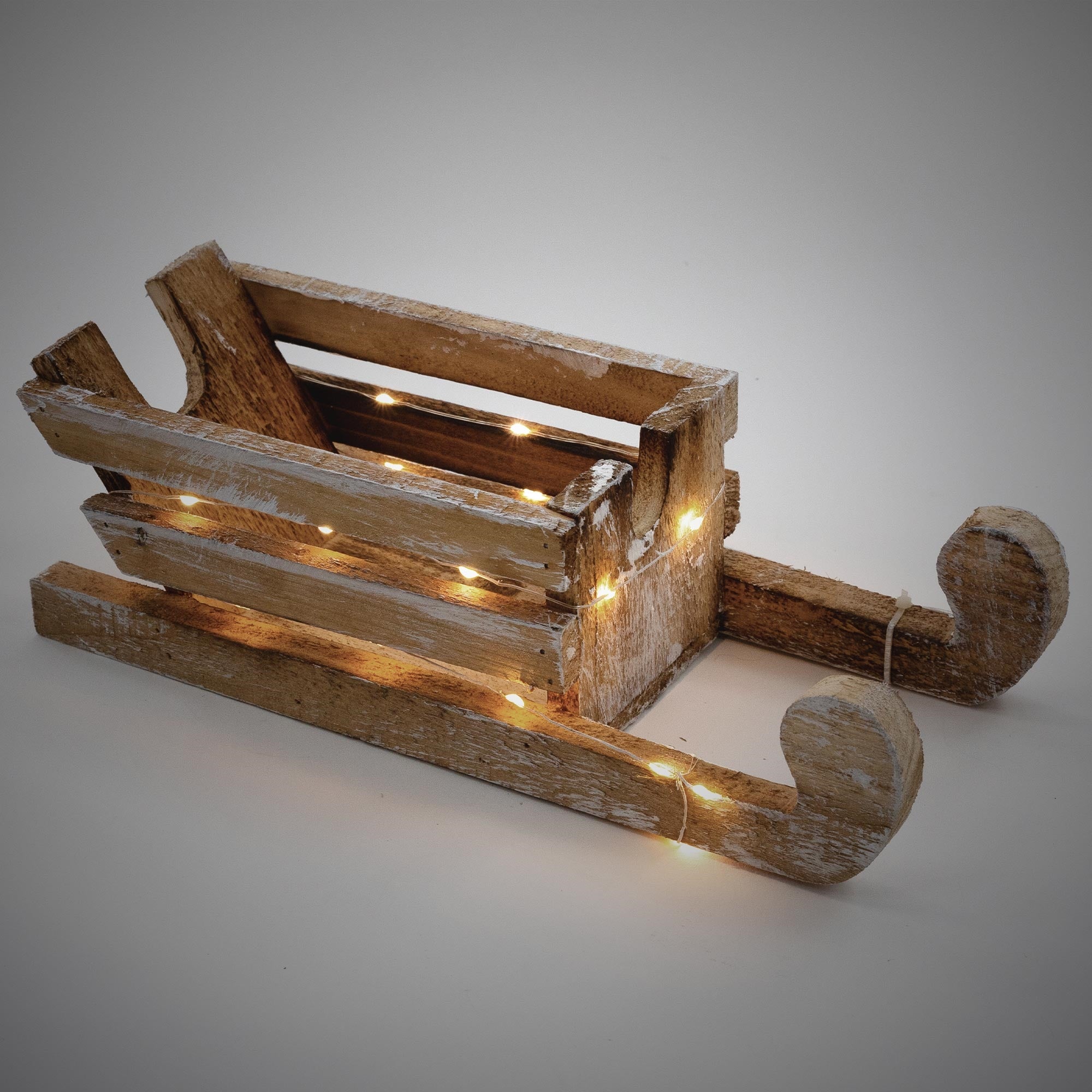 Holzschlitten mit Lichtern, auf grauem Hintergrund, in rustikalem Stil.