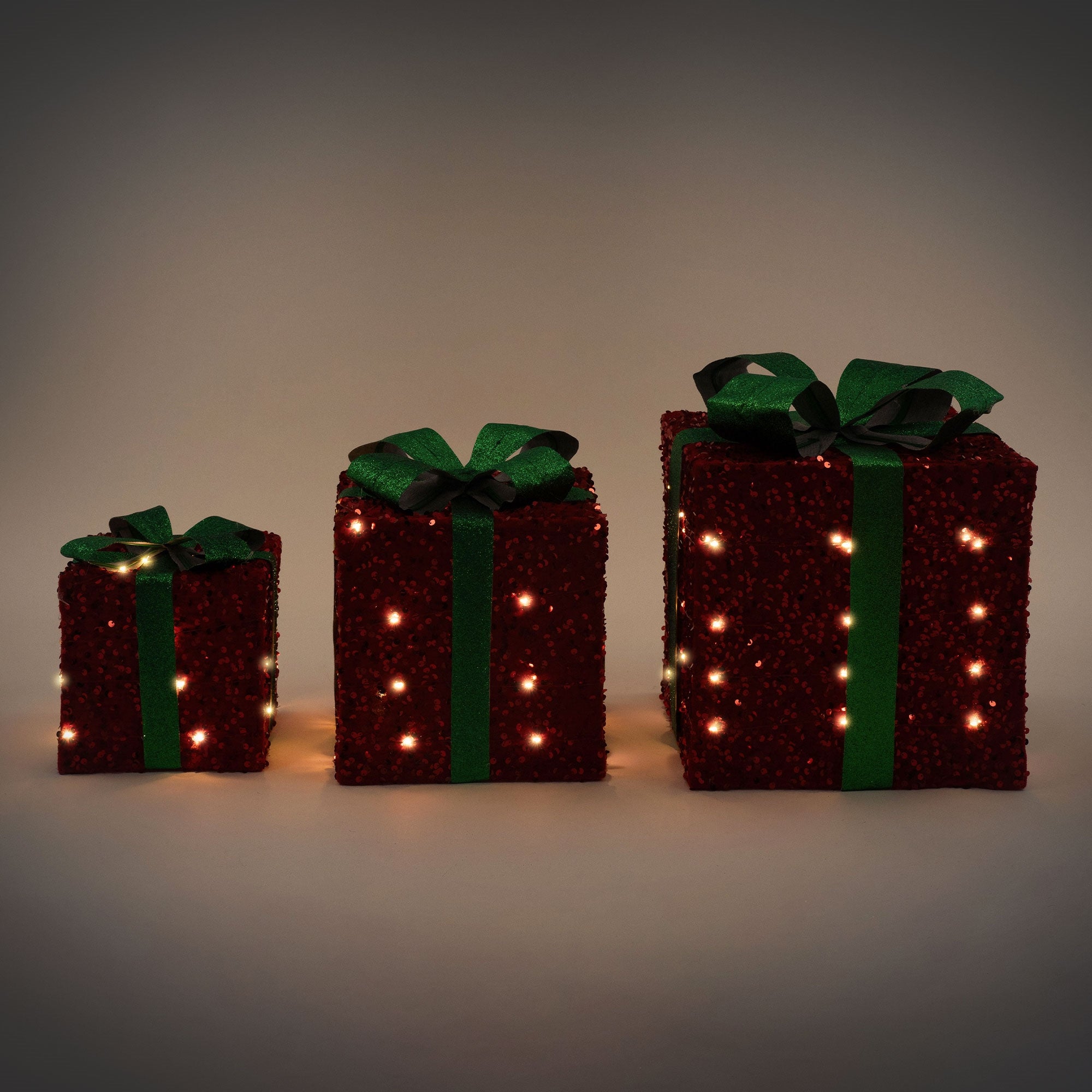 Tres regalos luminosos en diferentes tamaños con lazos verdes.