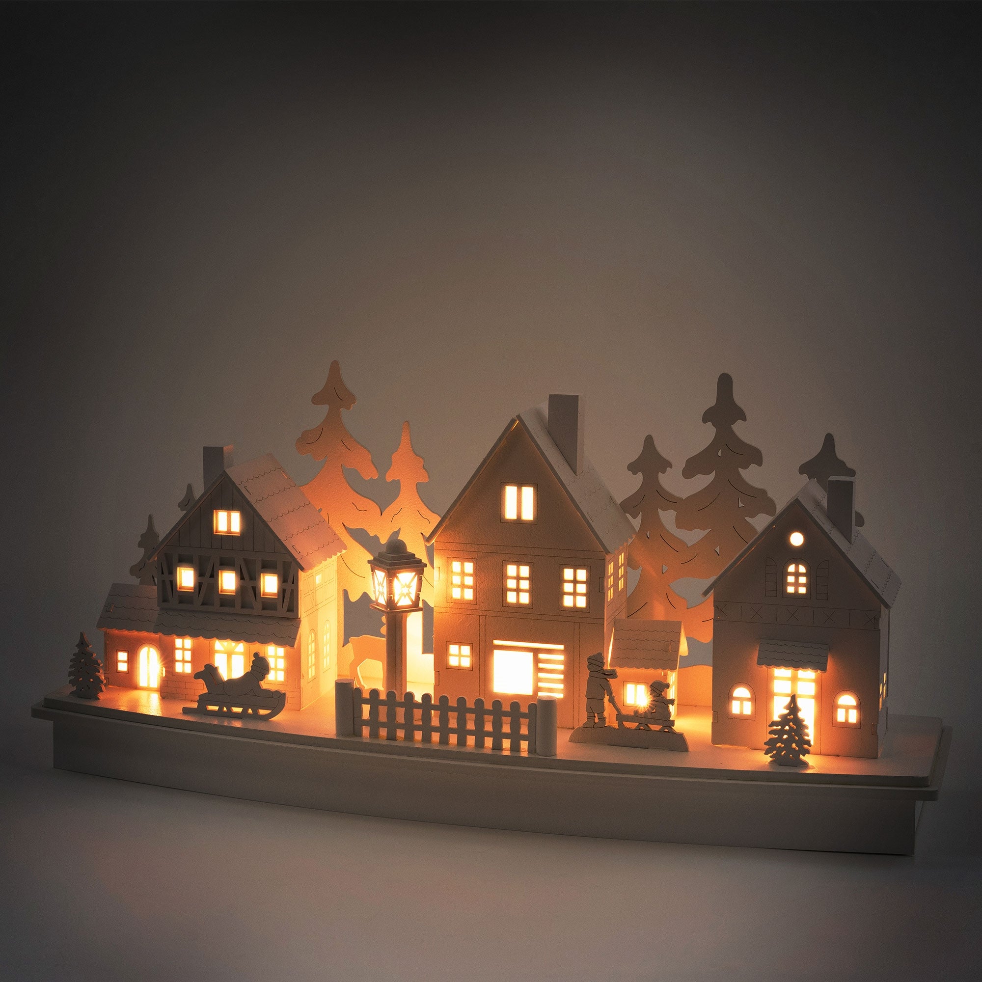 Maisons en carton éclairées et arbres sur une base décorative.