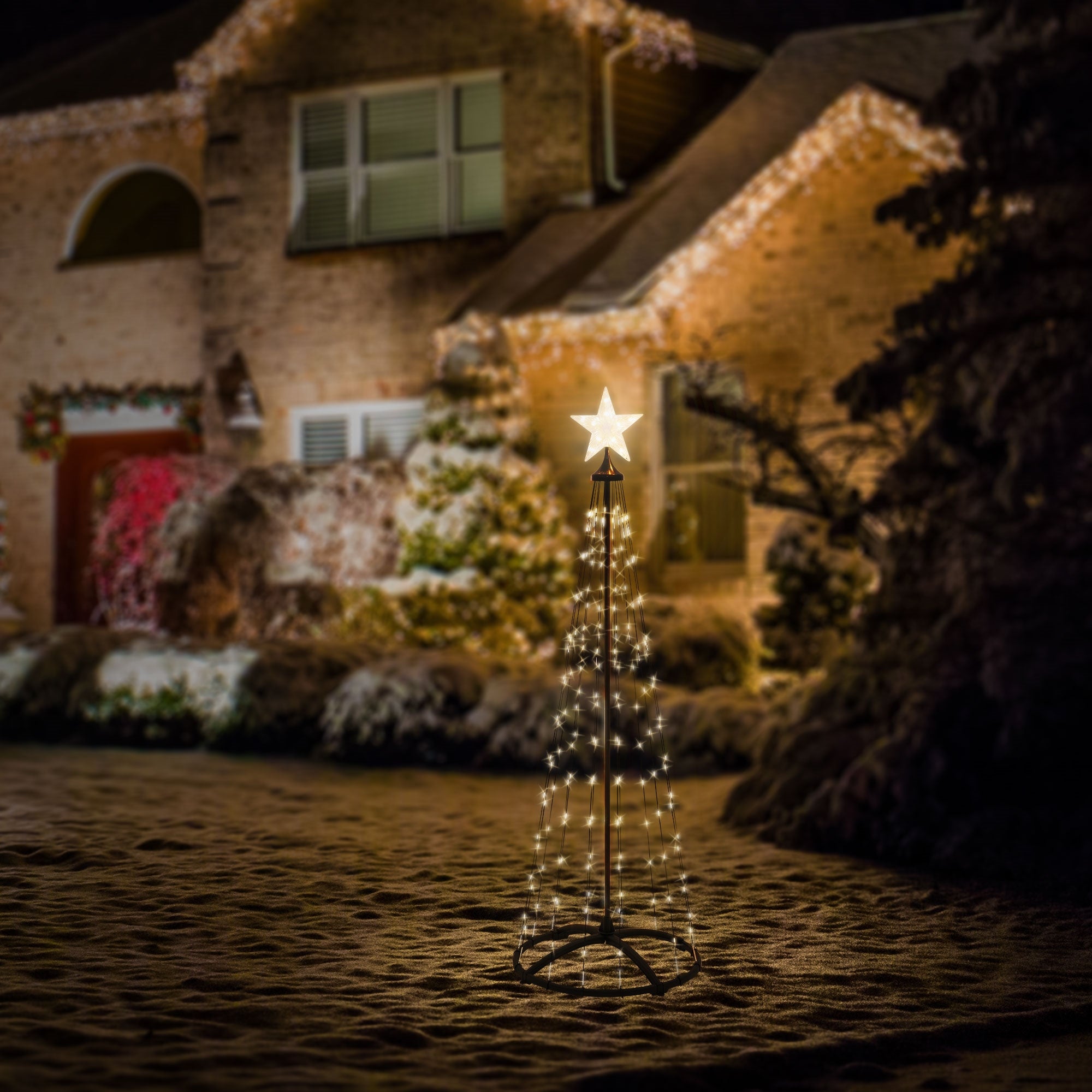 An illuminated Christmas tree with a star in front of a festively decorated house.