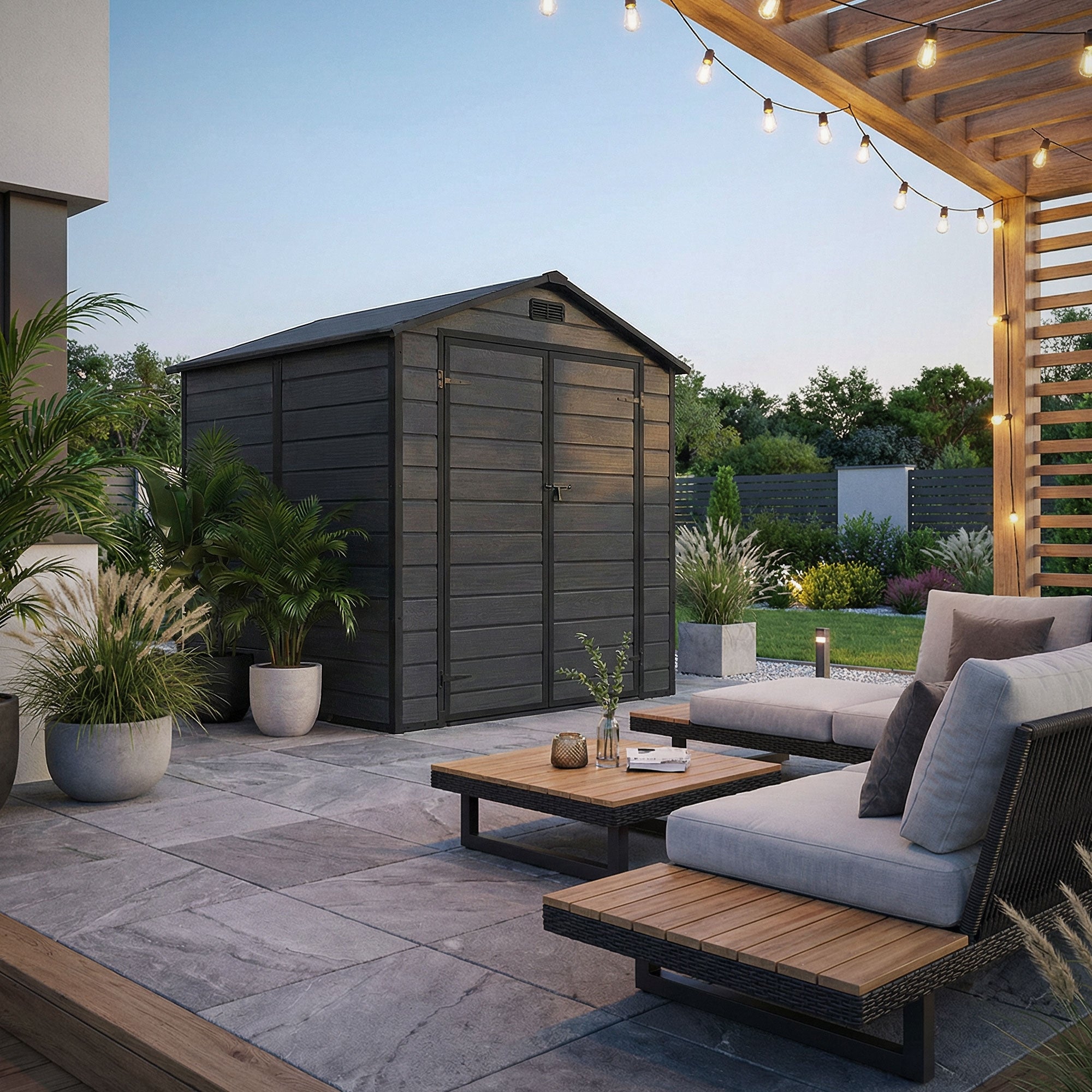 Houten schuur in de tuin, omgeven door planten en een terras met zitmeubelen.