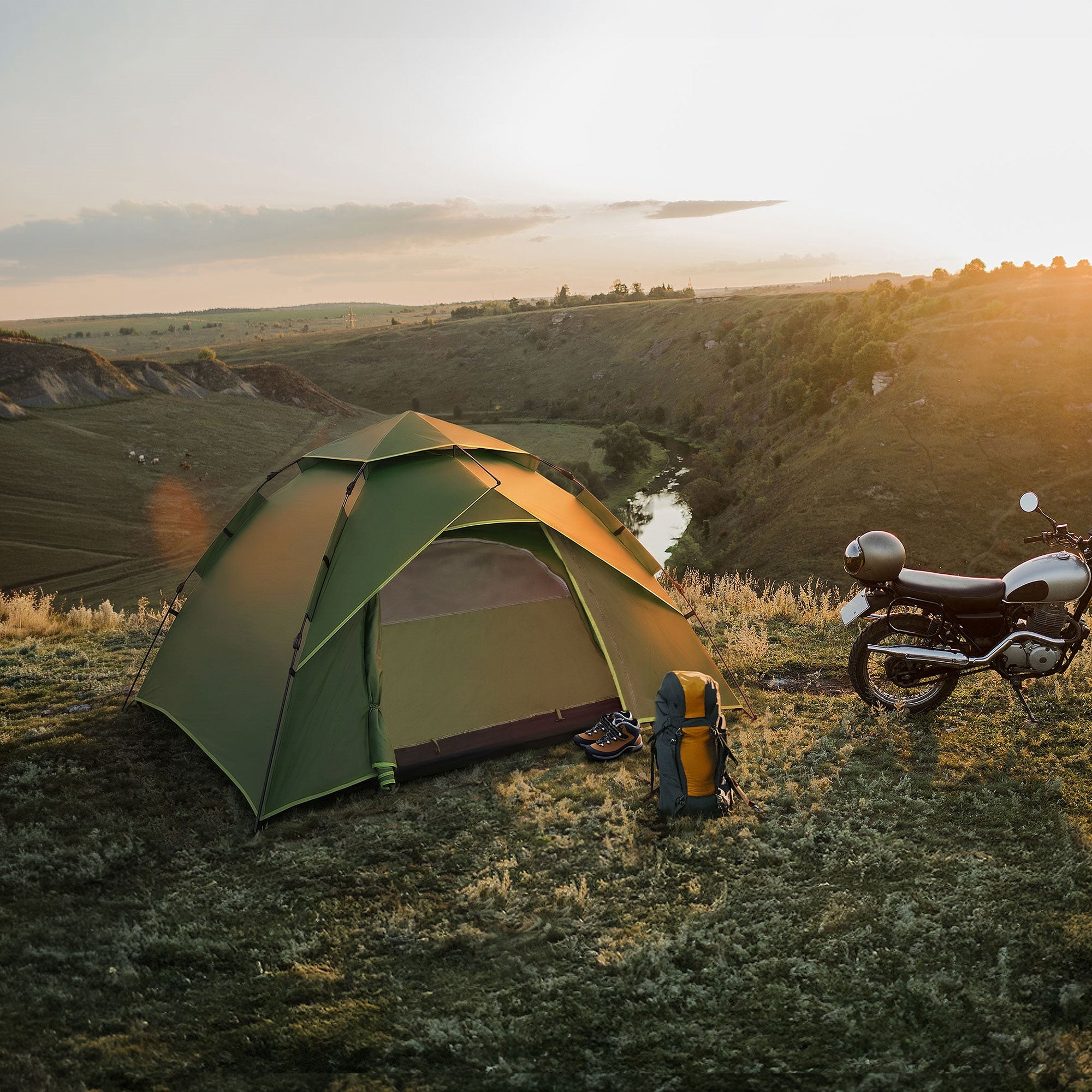 Tienda en la naturaleza al atardecer, con una mochila y una motocicleta cerca.
