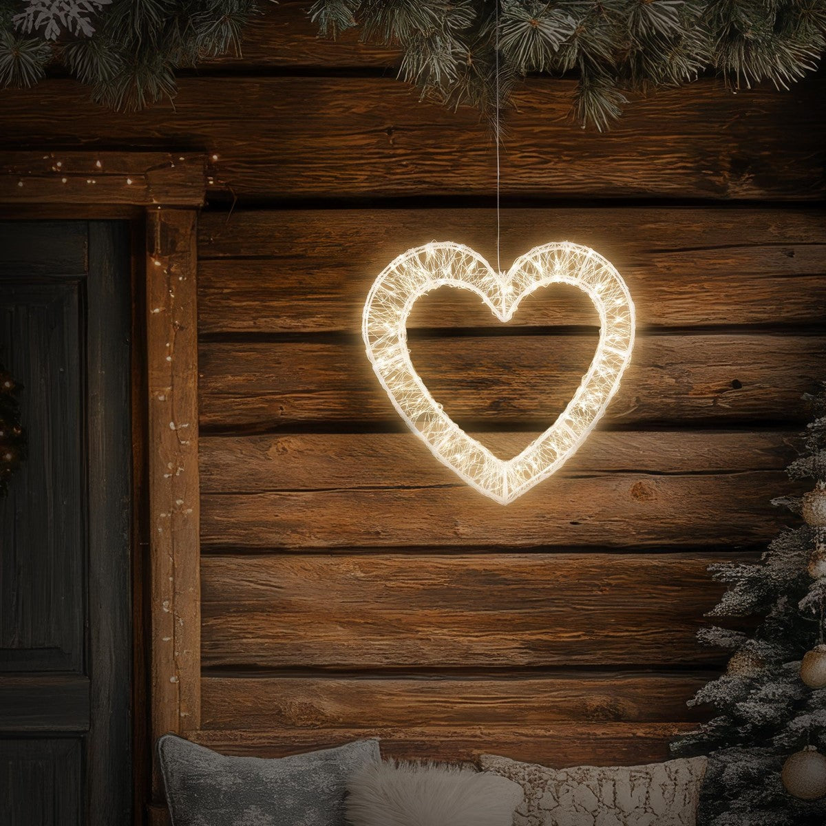 Leuchtendes Herz aus Lichtern, hängt an einer Holzwand neben einem Weihnachtsbaum.