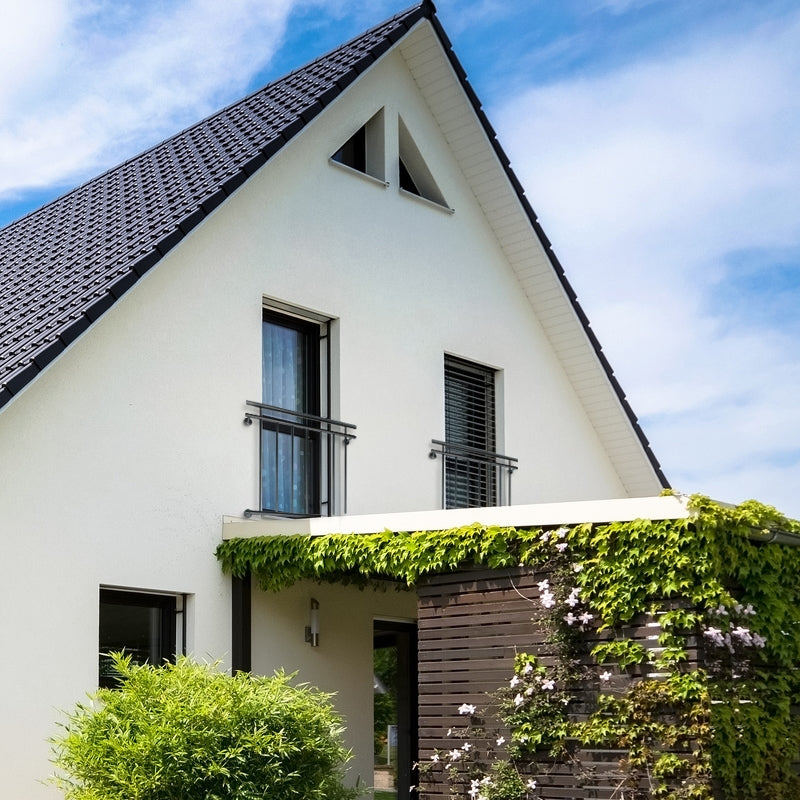 Maison avec un toit à deux pentes, des murs blancs et un espace d'entrée verdoyant.