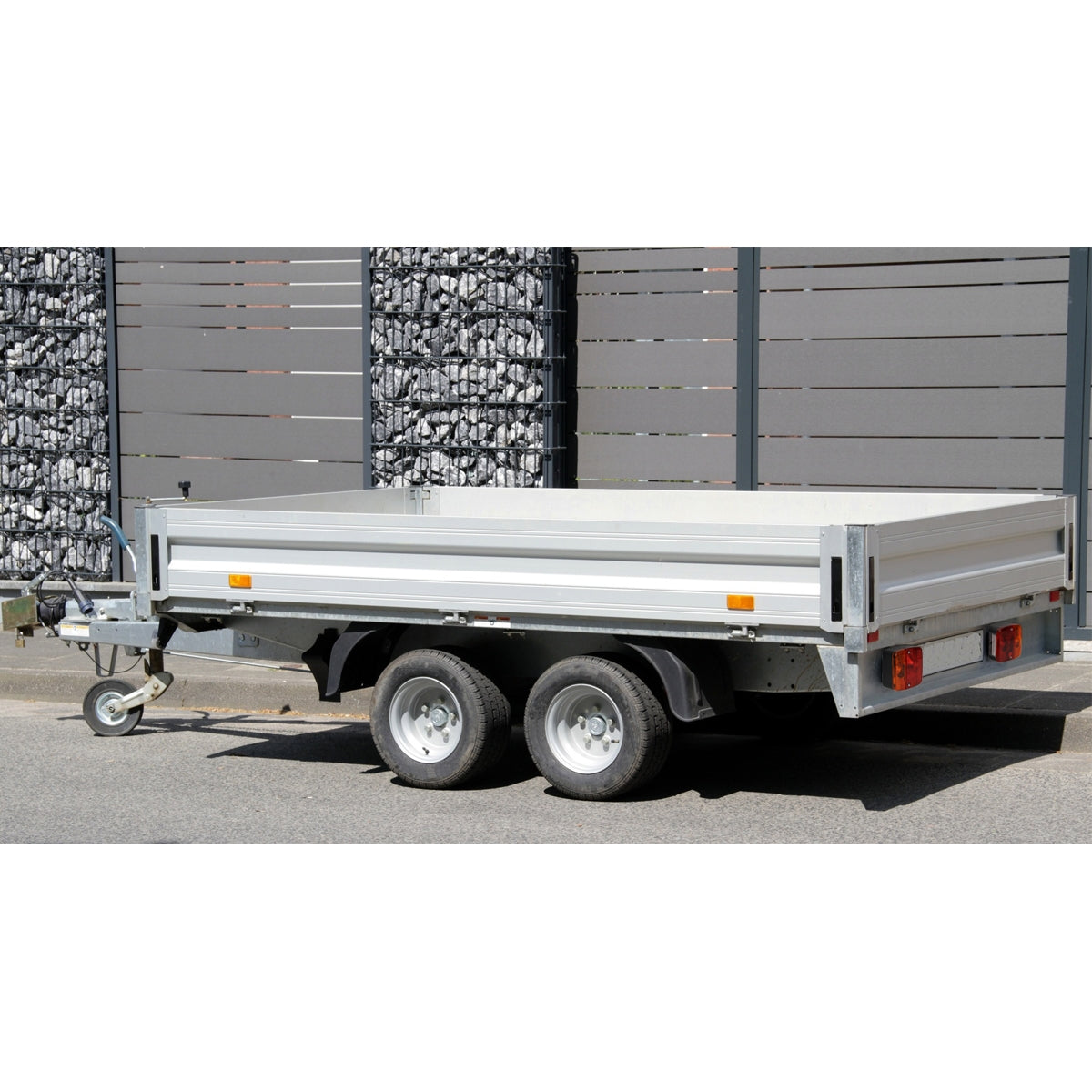A trailer with a flat loading area and two axles, parked on a road.