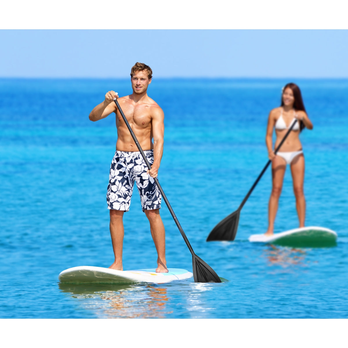 Dwie osoby wiosłują na stand-up paddleboardach w wodzie.