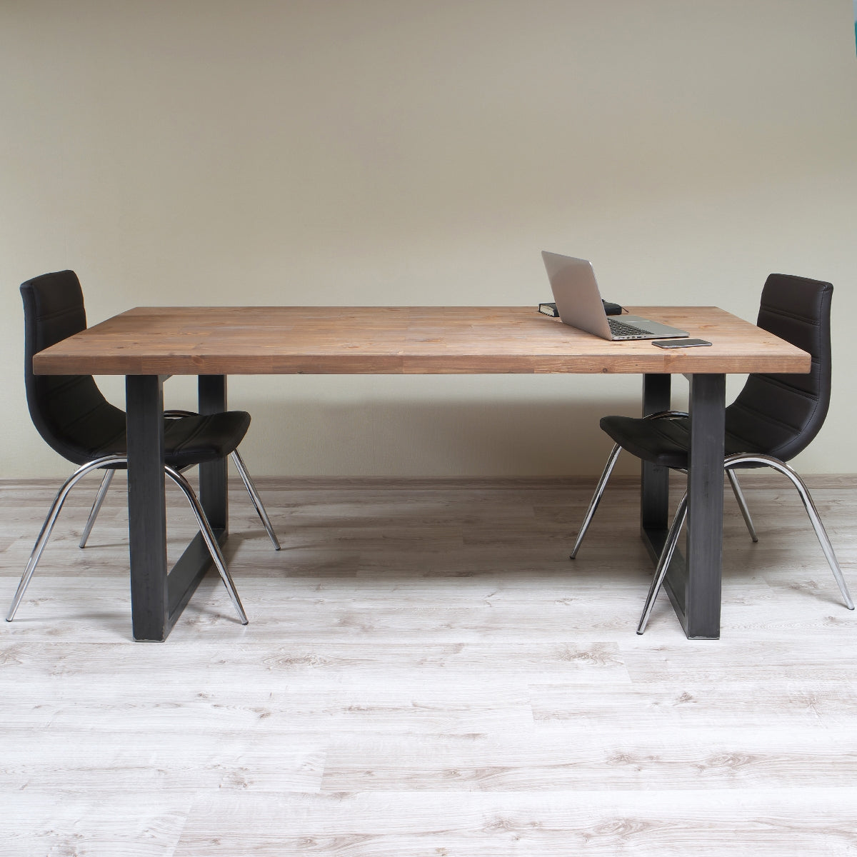 Holztisch mit Laptop und zwei schwarzen Stühlen, auf hellem Boden.