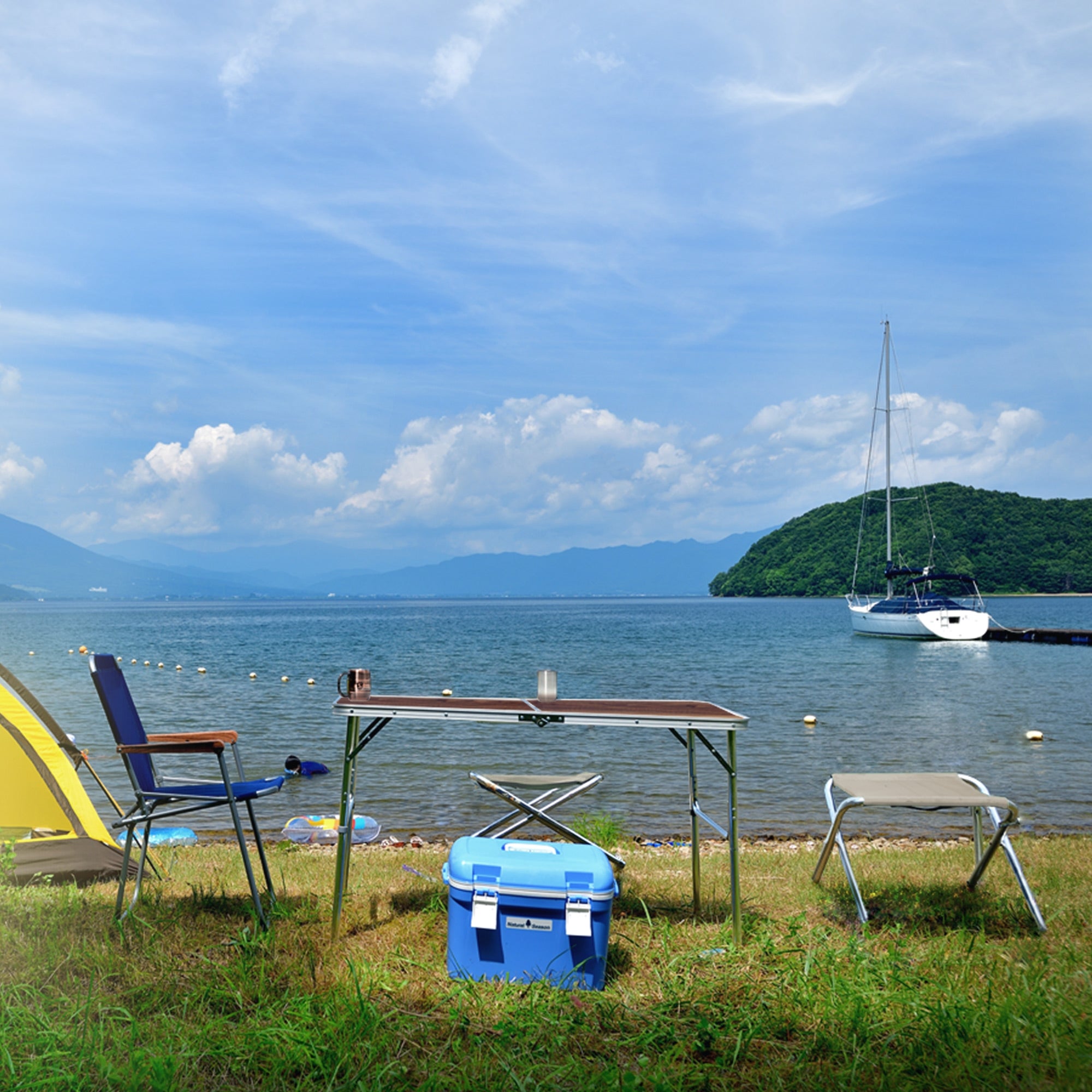Tisch und Stühle am Ufer eines Sees, mit Boot im Hintergrund.