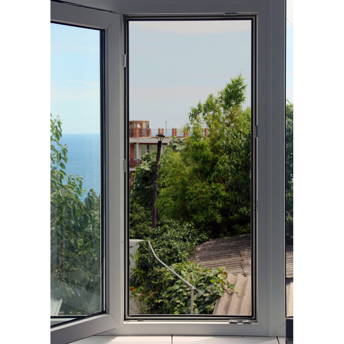 Offenes Fenster mit Blick auf einen grünen Garten und das Meer.